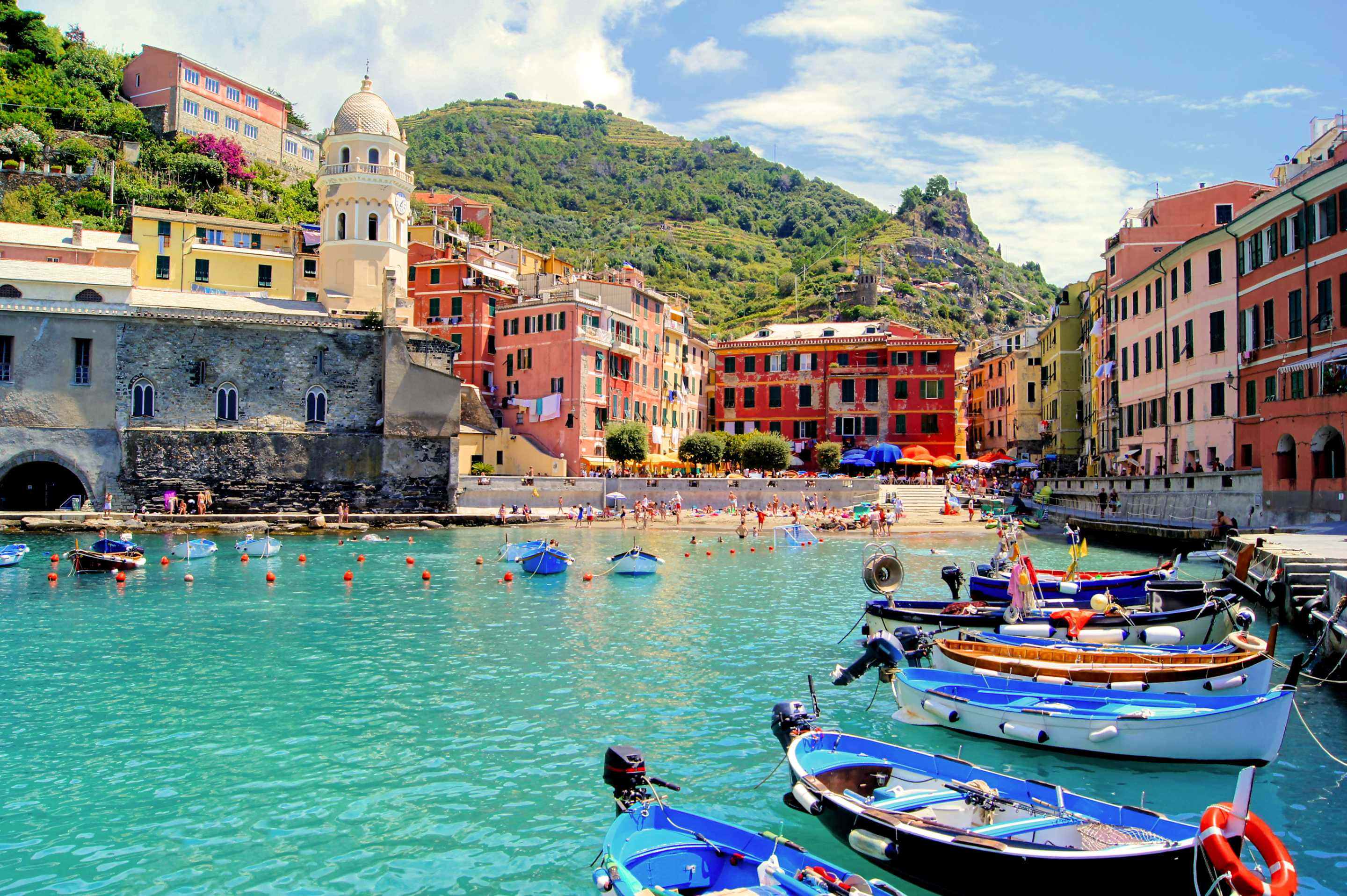 Italian Beach 桌布 壁紙 — 充滿活力的沿海村莊，色彩繽紛的建築物坐落在山丘上，俯瞰著點綴著小船的海藍寶石色海水。