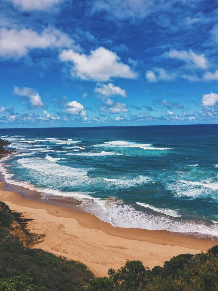 Australia Beach 桌布 壁紙 — 充滿活力的海岸景色，碧綠色的海浪拍打著金色沙灘，明亮的藍天點綴著蓬鬆的白雲。