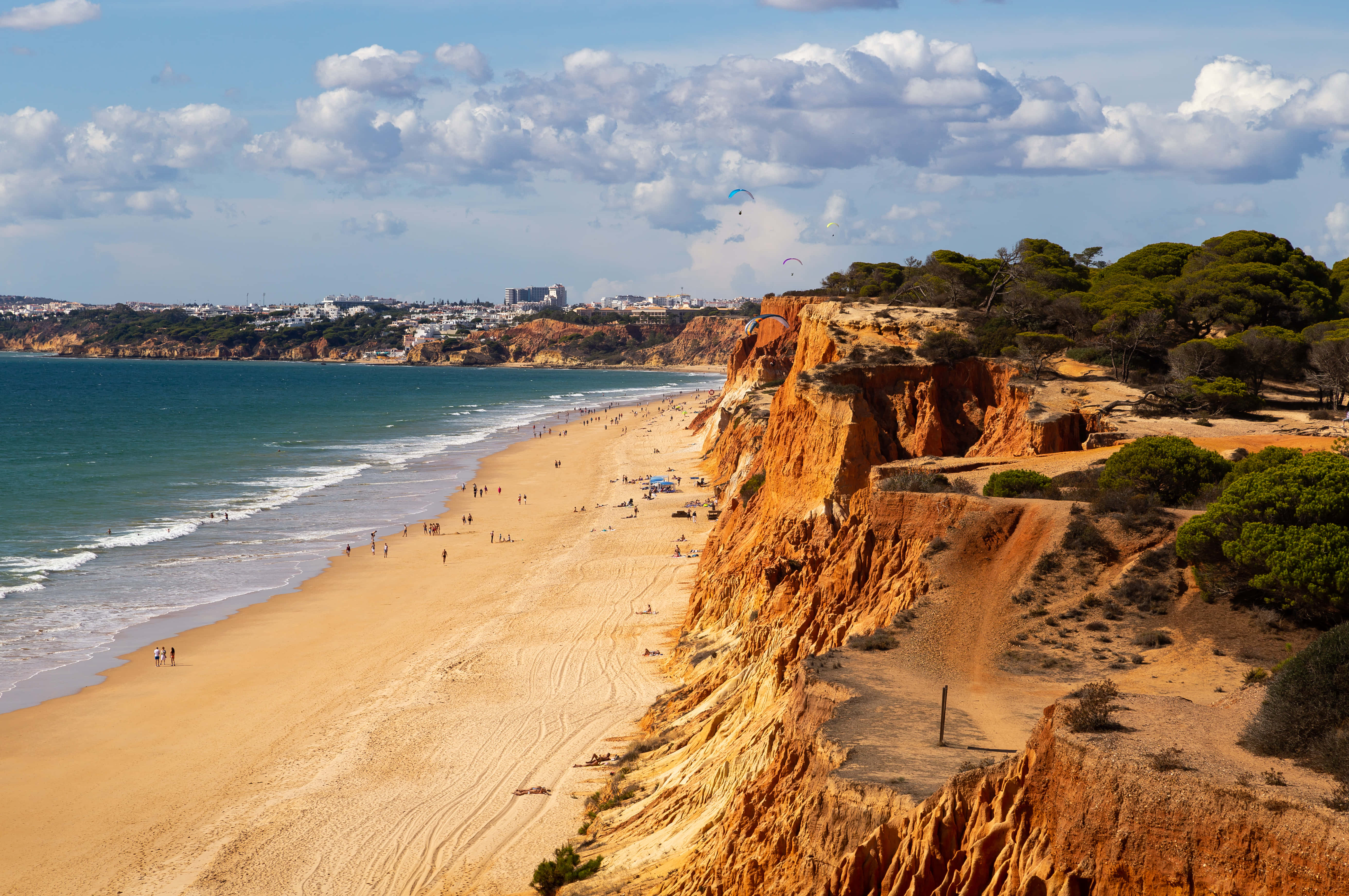 Portuguese Beach 桌布 壁紙 — 充滿活力的海灘場景，金色沙灘、碧綠海浪和戲劇性的橙色懸崖，天空部分多雲。