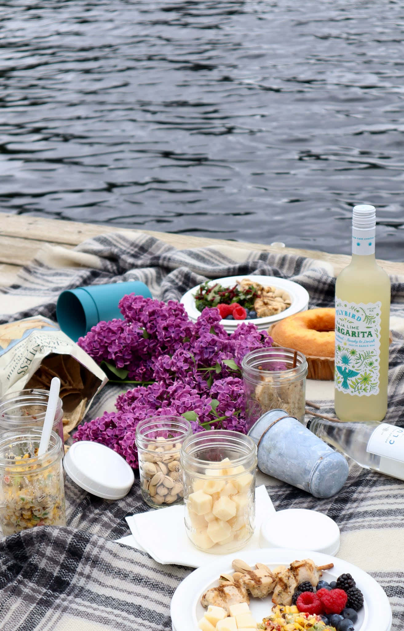 Beach Picnic 桌布 壁紙 — 充滿活力的湖邊野餐，有紫色丁香花、烤雞和瑪格麗特酒，鋪在格仔毯上。