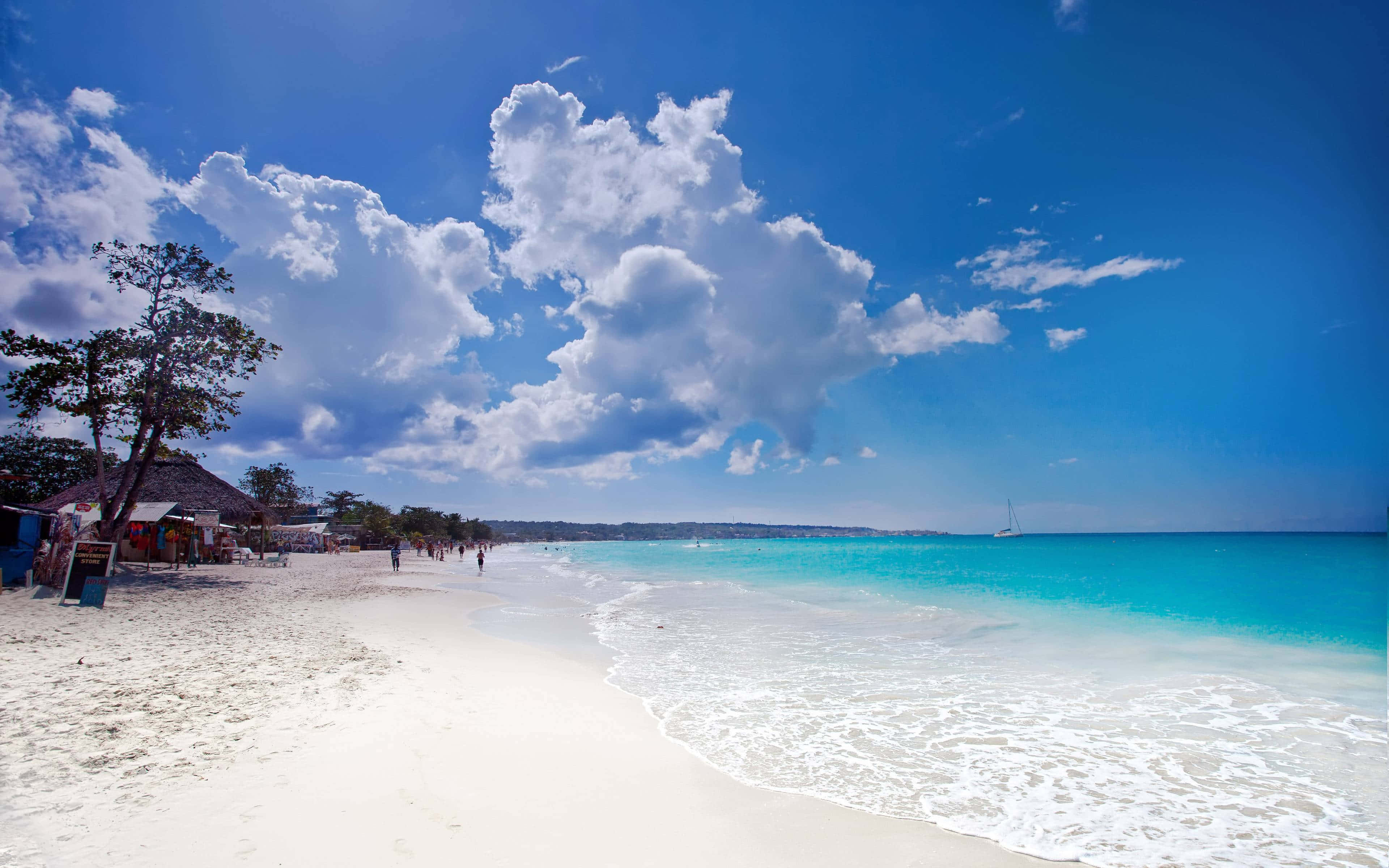 Jamaica 桌布 壁紙 — 充滿活力的熱帶海灘，擁有碧綠的海水、溫柔的海浪、白色的沙灘和蓬鬆的雲朵，在明亮的藍天下。