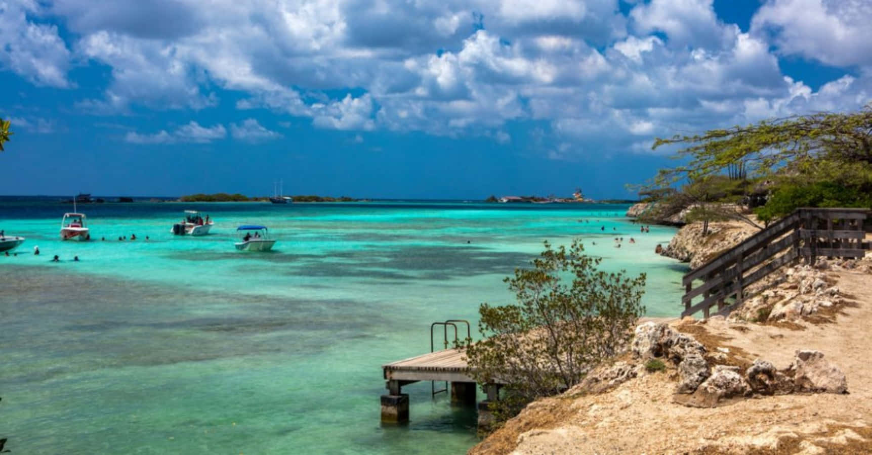 Aruba 桌布 壁紙 — 充滿活力的碧綠海水中有游泳者和船隻，天空蔚藍，白雲朵朵。
