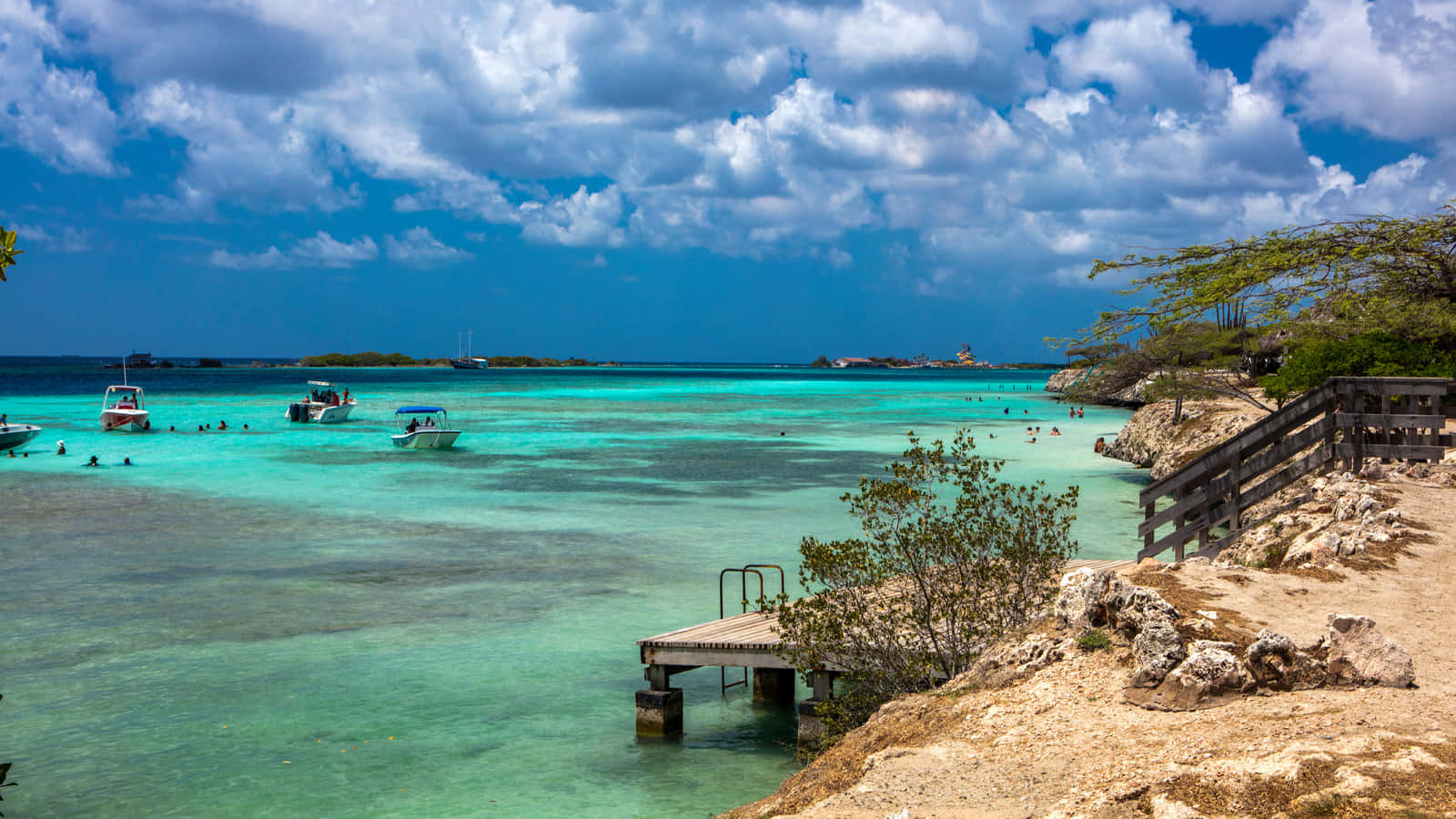 Aruba 桌布 壁紙 — 充滿活力的碧綠海水中有游泳者和船隻，在戲劇性的藍天和蓬鬆的白雲下。