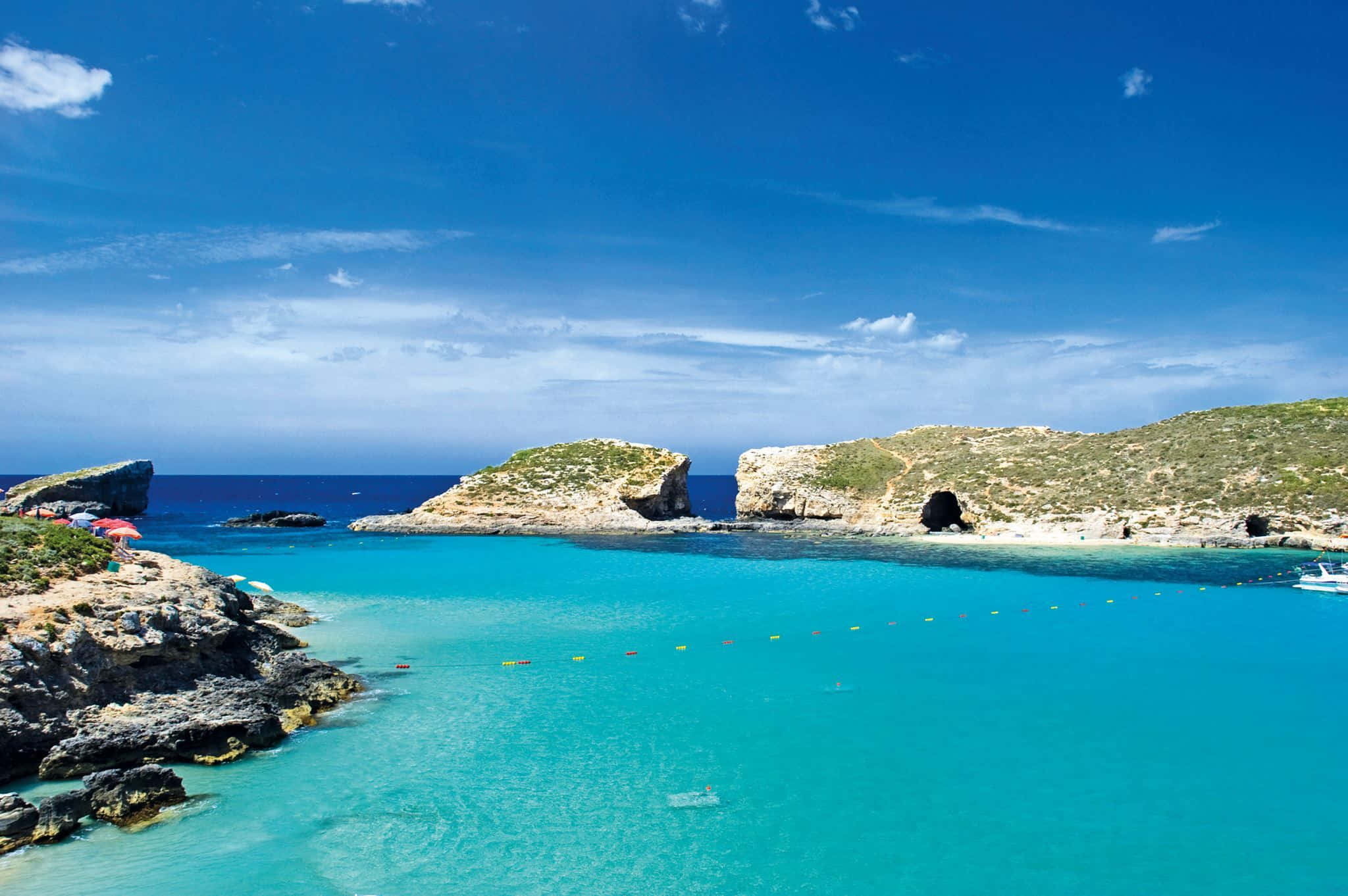 Malta 桌布 壁紙 — 充滿活力的碧綠海水環抱著一個僻靜的小海灣，四周是崎嶇的懸崖，上方是明亮的藍天，點綴著縷縷白雲。