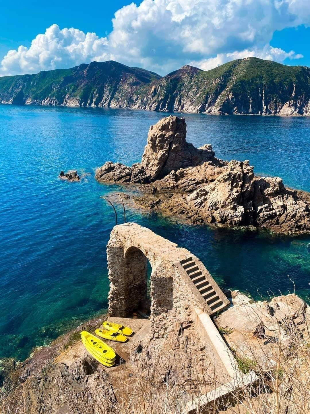 4K 桌布 壁紙 — 充滿活力的碧綠海水環繞著古老的石頭遺跡，黃色皮划艇在明亮的藍天下停靠在一旁。