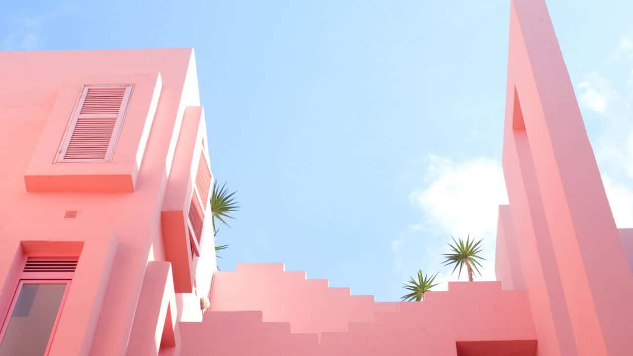 Pastel Minimalist 桌布 壁紙 — 充滿活力的粉紅色幾何建築在晴朗的藍天下聳立，稀疏的棕櫚樹探出頭來。