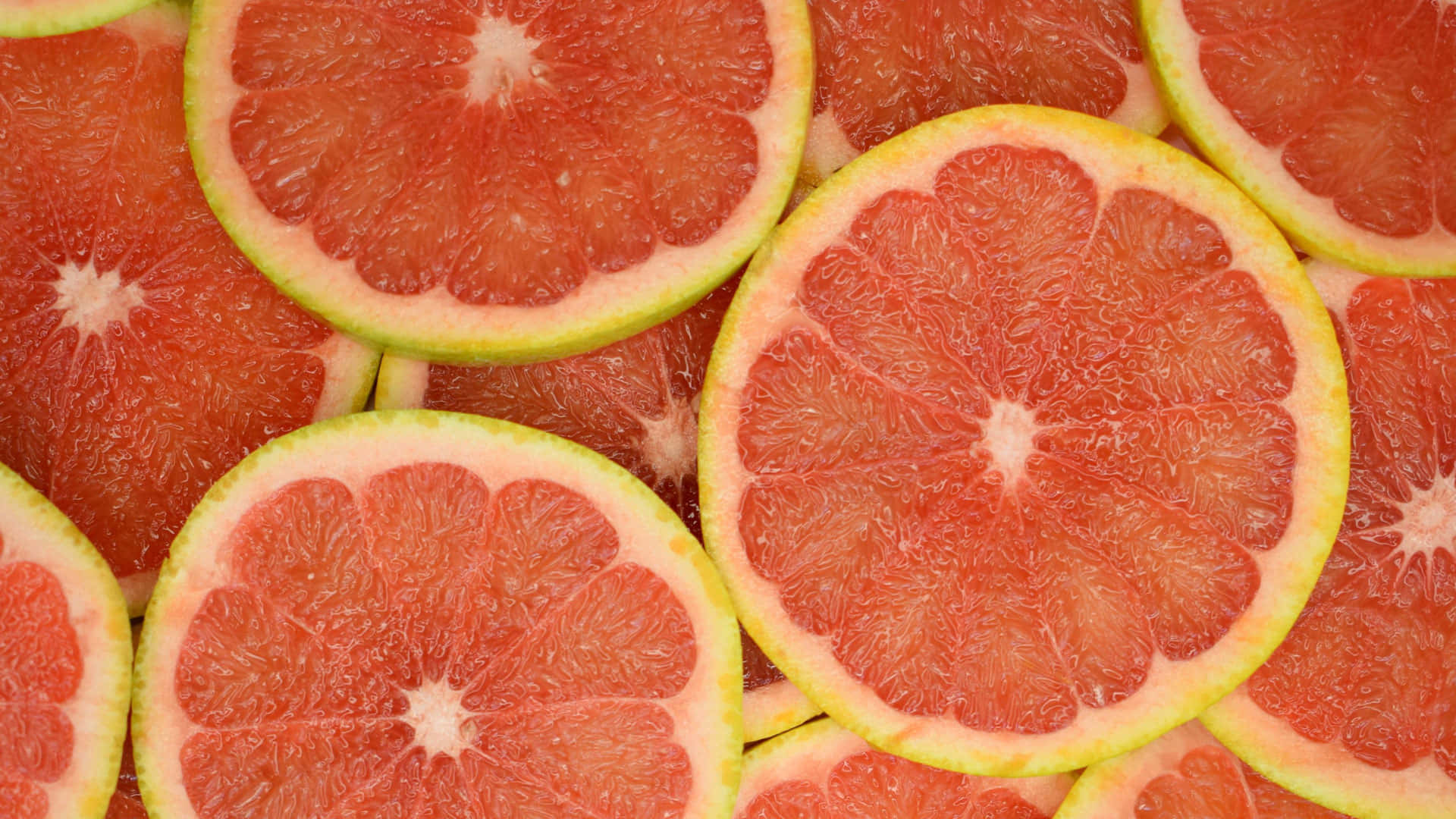 Pink Grapefruit 桌布 壁紙 — 充滿活力的粉紅西柚切片特寫，展現分瓣的果肉和淺色果皮。