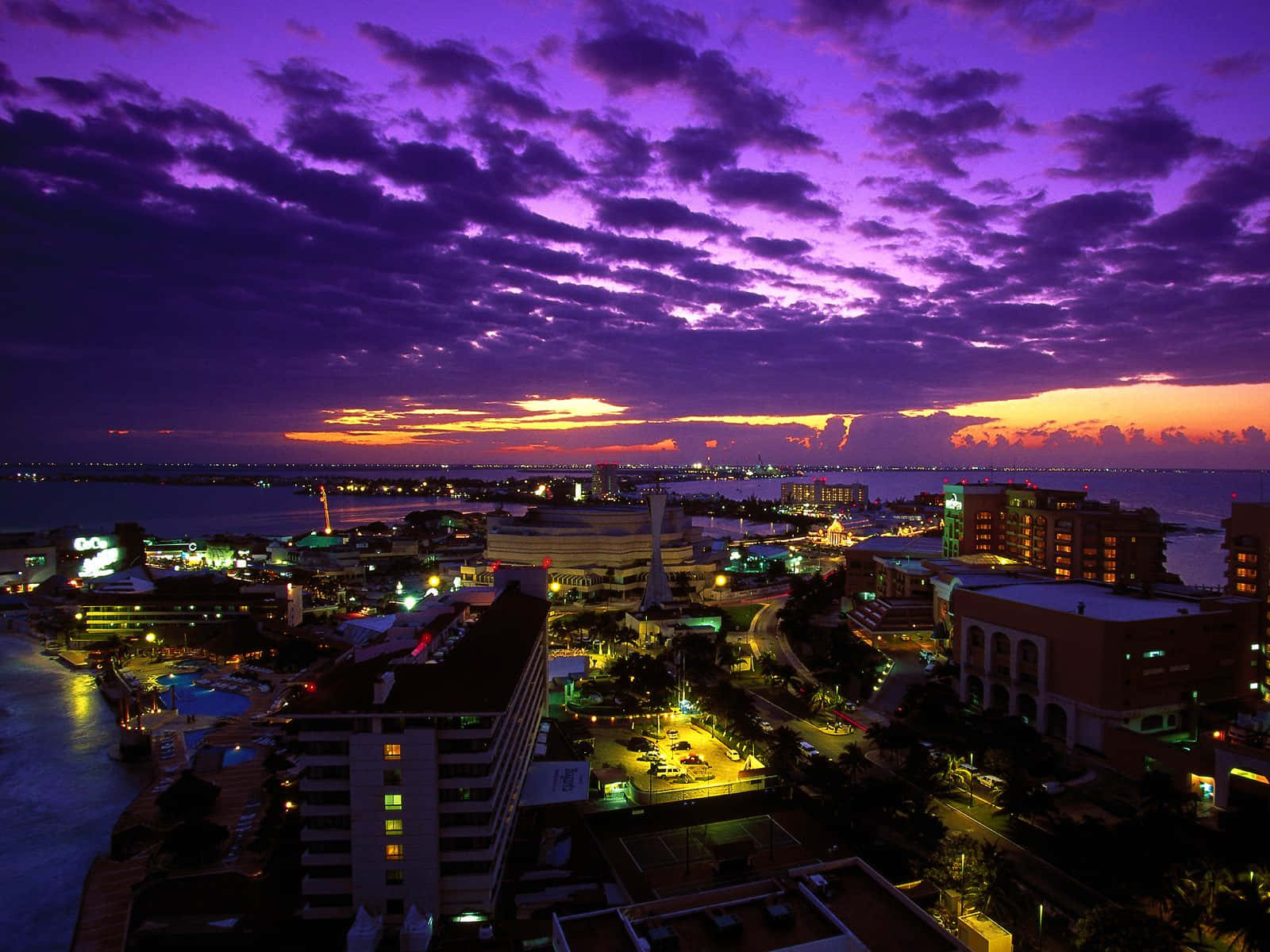 Beautiful City 桌布 壁紙 — 充滿活力的紫色和橙色日落照亮了沿海城市景觀，建築物和水中倒影閃閃發光。