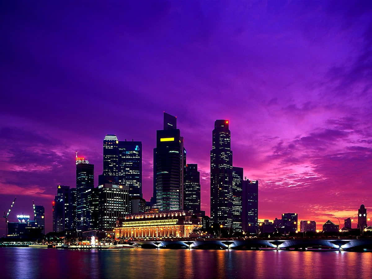 Singapore 桌布 壁紙 — 充滿活力的紫色和粉紅色日落照亮了新加坡的天際線，發光的摩天大樓倒映在平靜的水面上。
