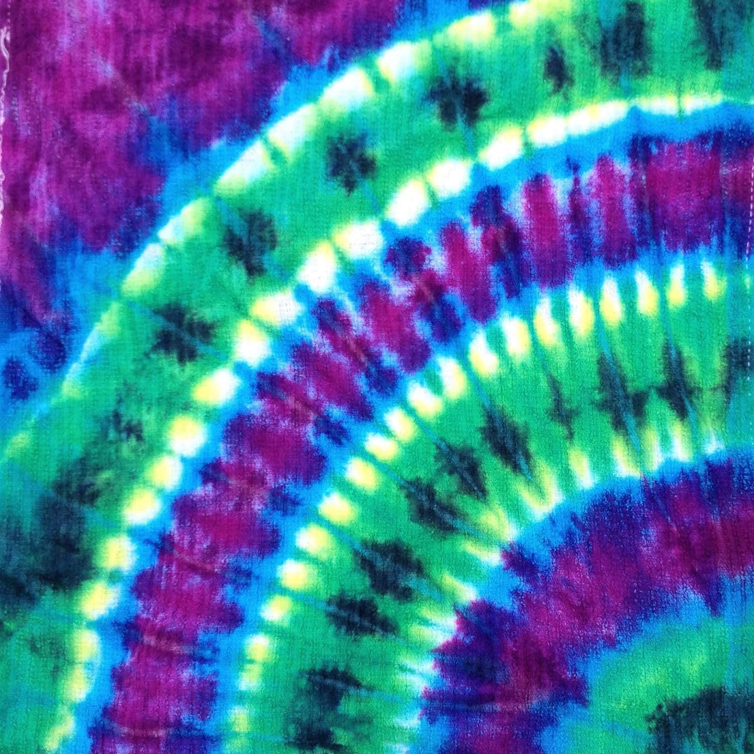 Purple Tie Dye 桌布 壁紙 — 充滿活力的紮染布料漩渦，呈現電光綠、紫色和藍色，並帶有霓虹黃亮點。