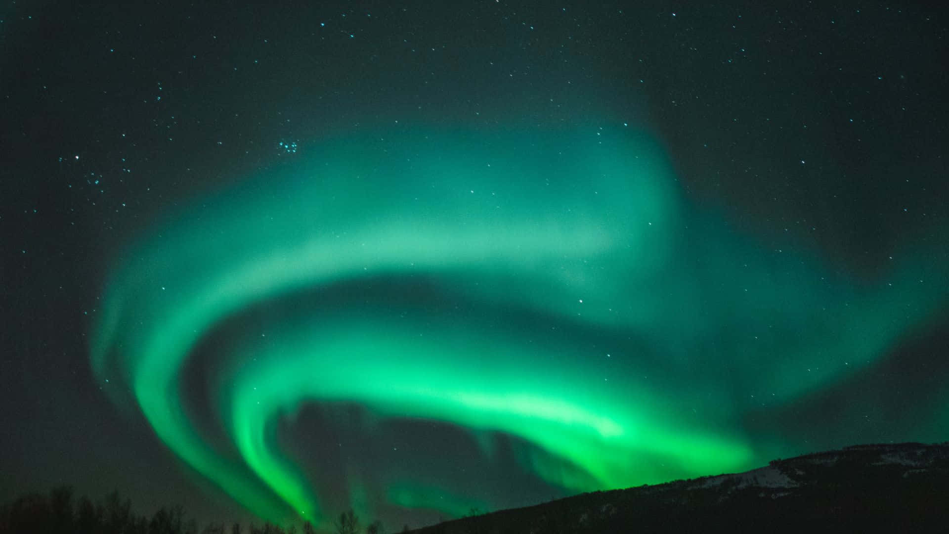 aurora borealis 桌布 壁紙 — 充滿活力的綠色北極光在繁星點點的夜空下，在積雪的山脊上舞動。