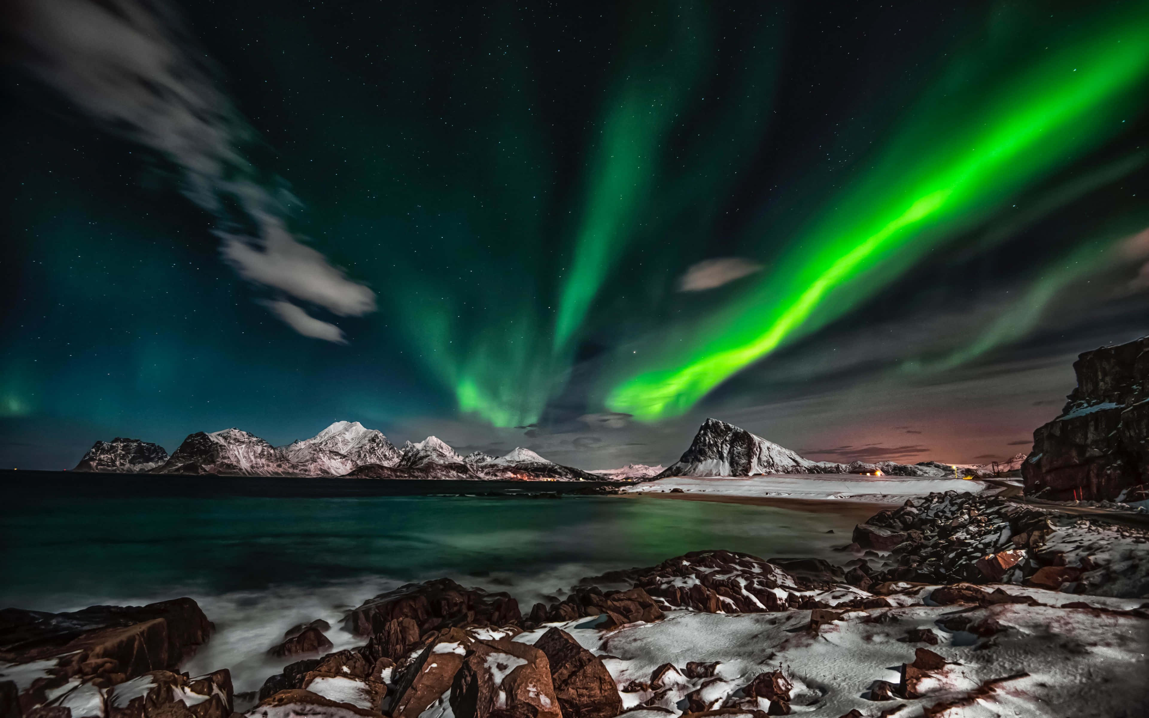 aurora borealis 桌布 壁紙 — 充滿活力的綠色北極光在繁星點點的夜空中舞動，下方是白雪覆蓋的山脈和寧靜的大海。