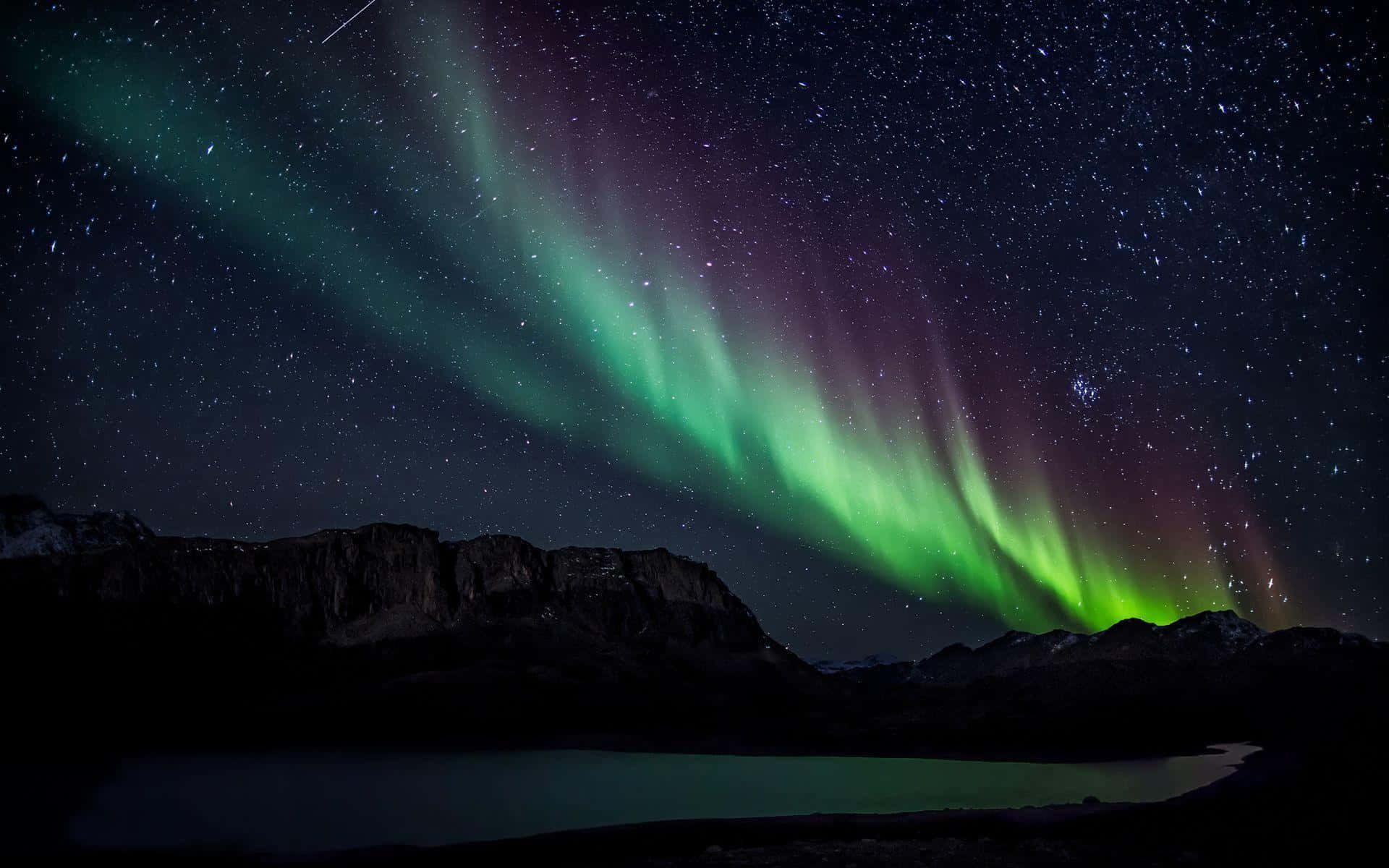 aurora borealis 桌布 壁紙 — 充滿活力的綠色和紫色北極光在繁星點點的夜空中，在黑暗的山脈輪廓和寧靜的湖泊上方舞動。