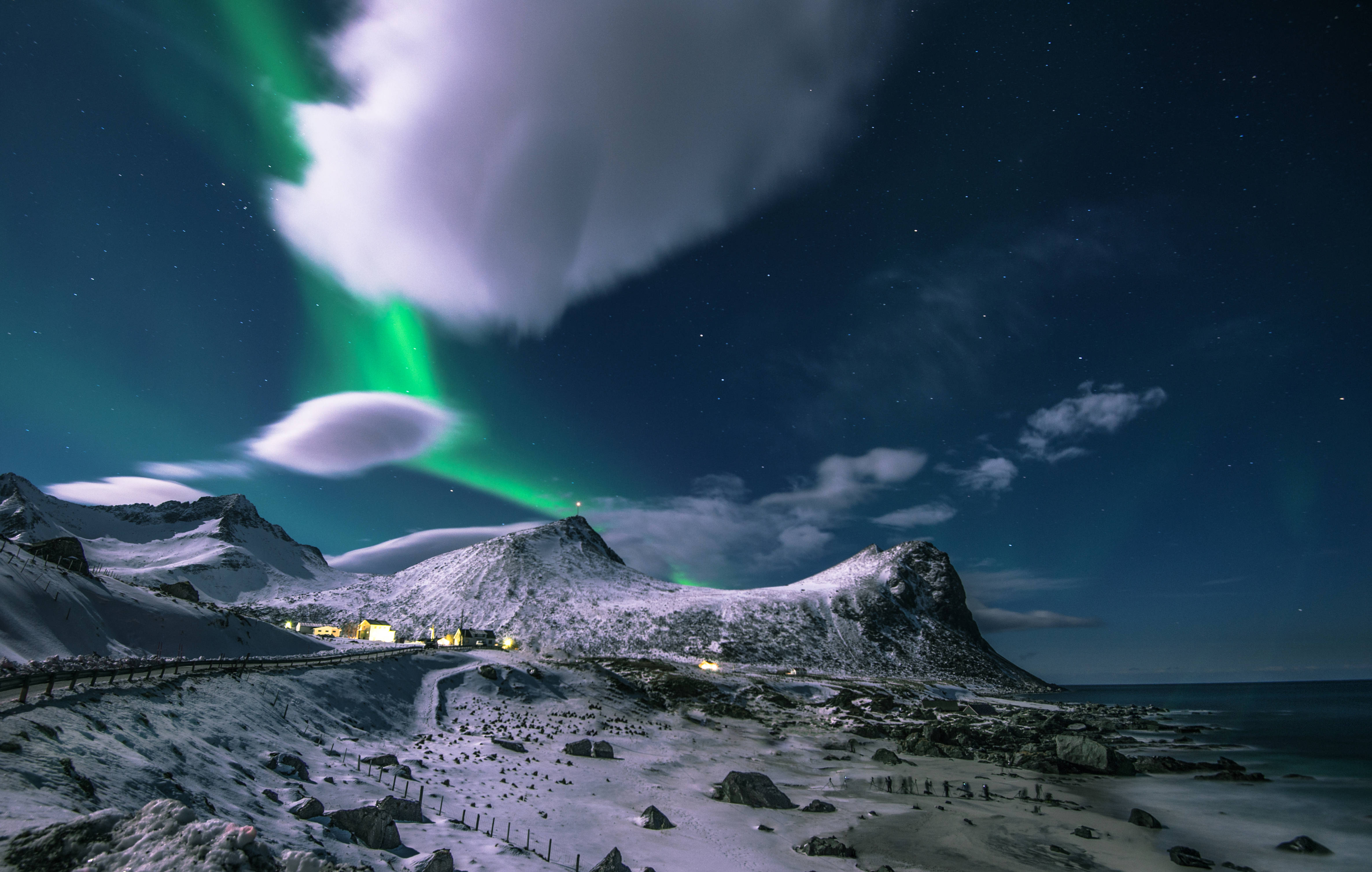 Norway 桌布 壁紙 — 充滿活力的綠色極光在星空下舞動於白雪覆蓋的山脈和沿海村莊之上。