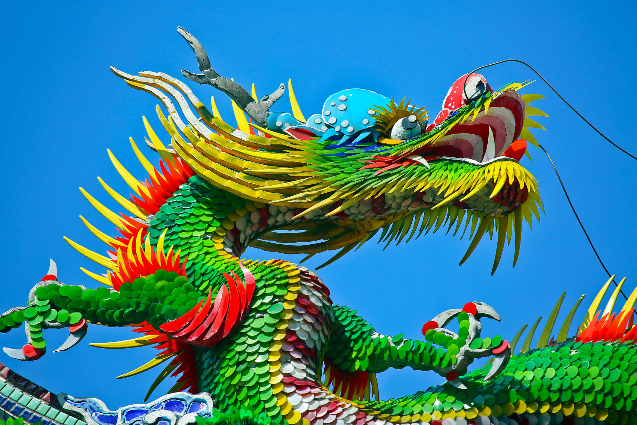 Dragons 桌布 壁紙 — 充滿活力的綠色龍雕塑，帶有火紅和黃色點綴，映襯著清澈的藍天。
