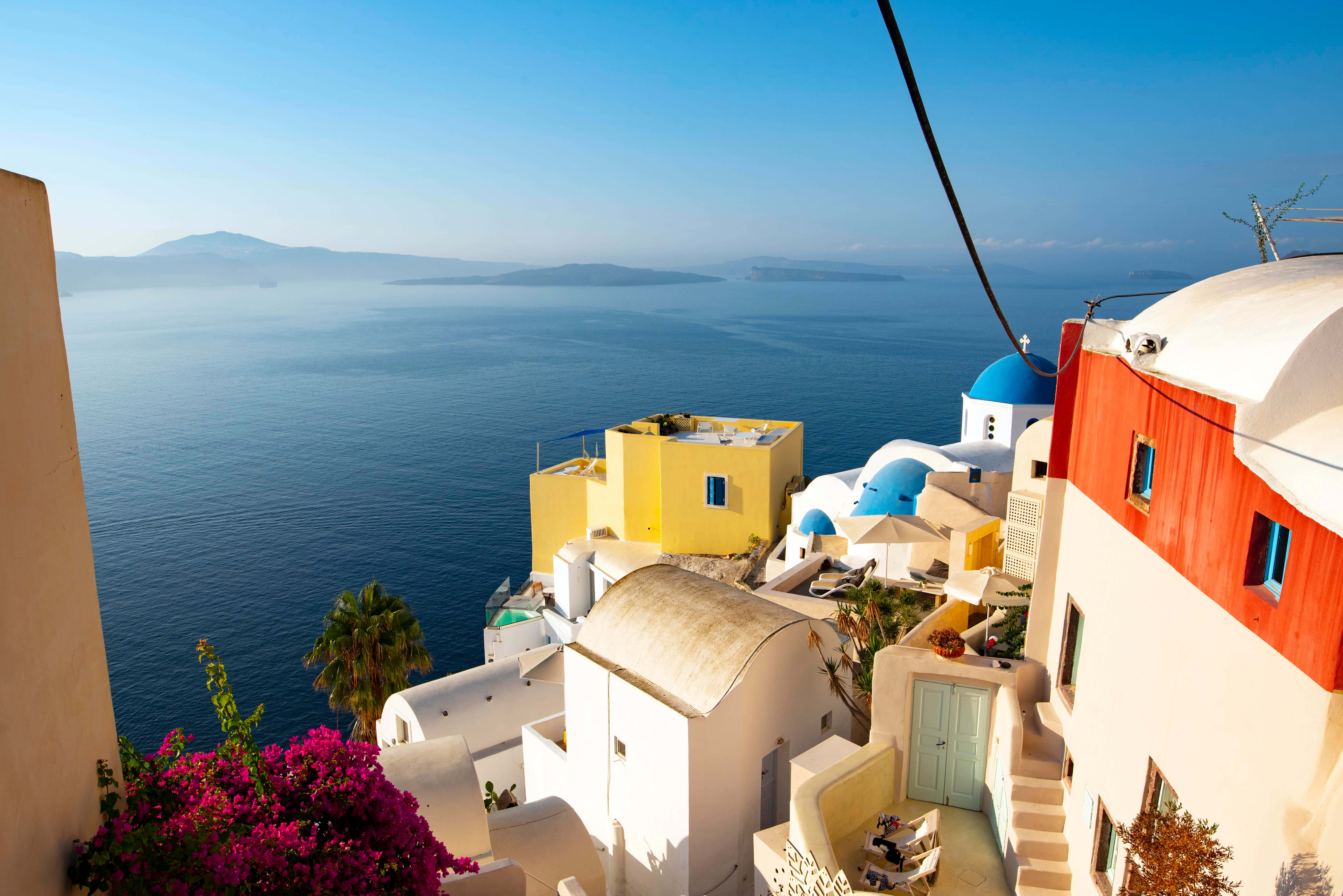 Greek Island 桌布 壁紙 — 充滿活力的聖托里尼懸崖村莊，擁有白色圓頂教堂和色彩繽紛的建築，俯瞰深藍色的愛琴海。