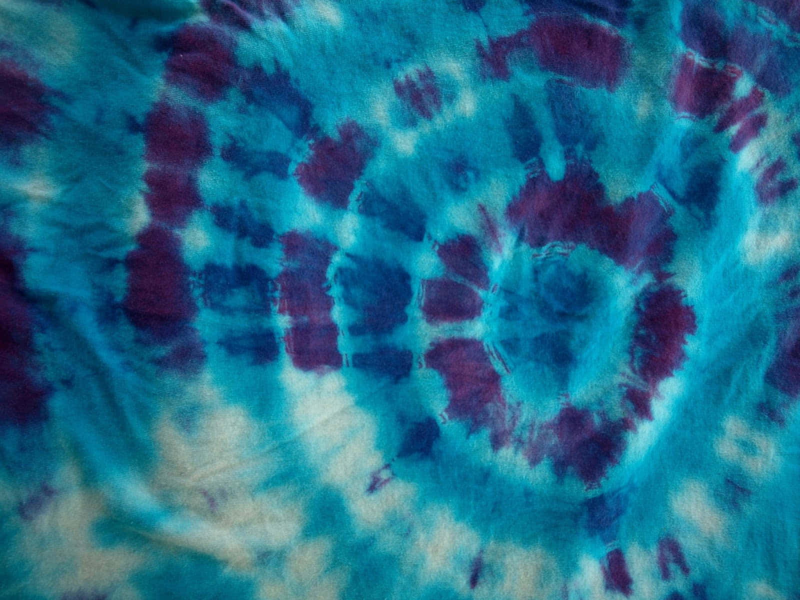 Purple Tie Dye 桌布 壁紙 — 充滿活力的藍色和紫色紮染布料特寫，帶有漩渦圖案和柔和的白色點綴。