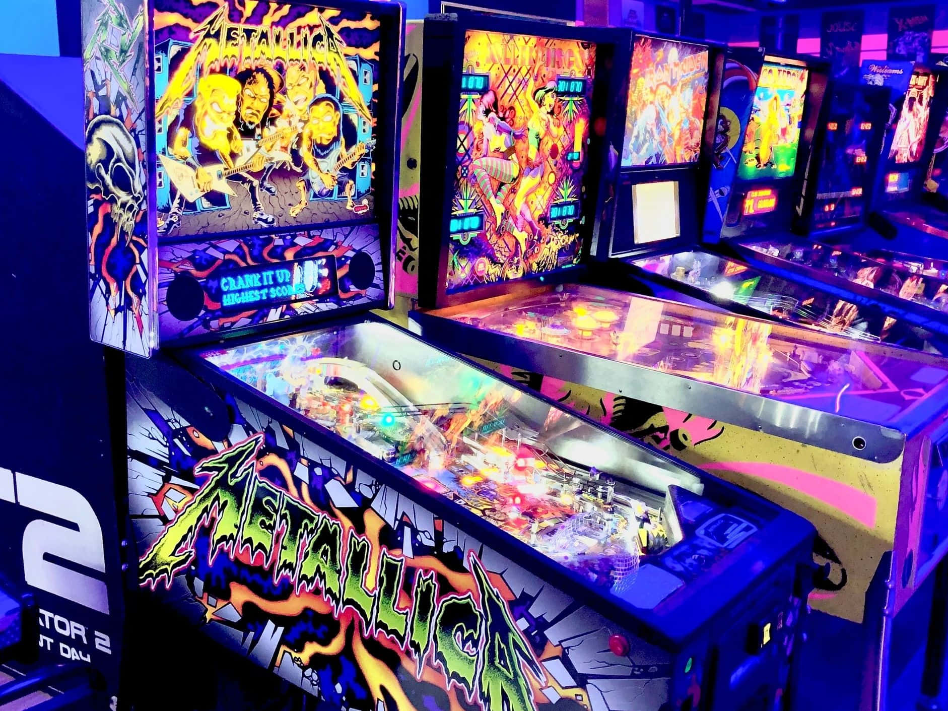 Arcade Games 桌布 壁紙 — 充滿活力的霓虹燈彈珠機，帶有Metallica藝術作品，在充滿彩色燈光和閃爍顯示屏的復古遊戲廳中發光。
