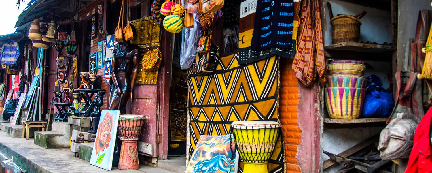 Liberia 桌布 壁紙 — 充滿活力的非洲手工藝品和紡織品在熙攘的戶外市場攤位中展示，配有色彩繽紛的鼓和編織籃。