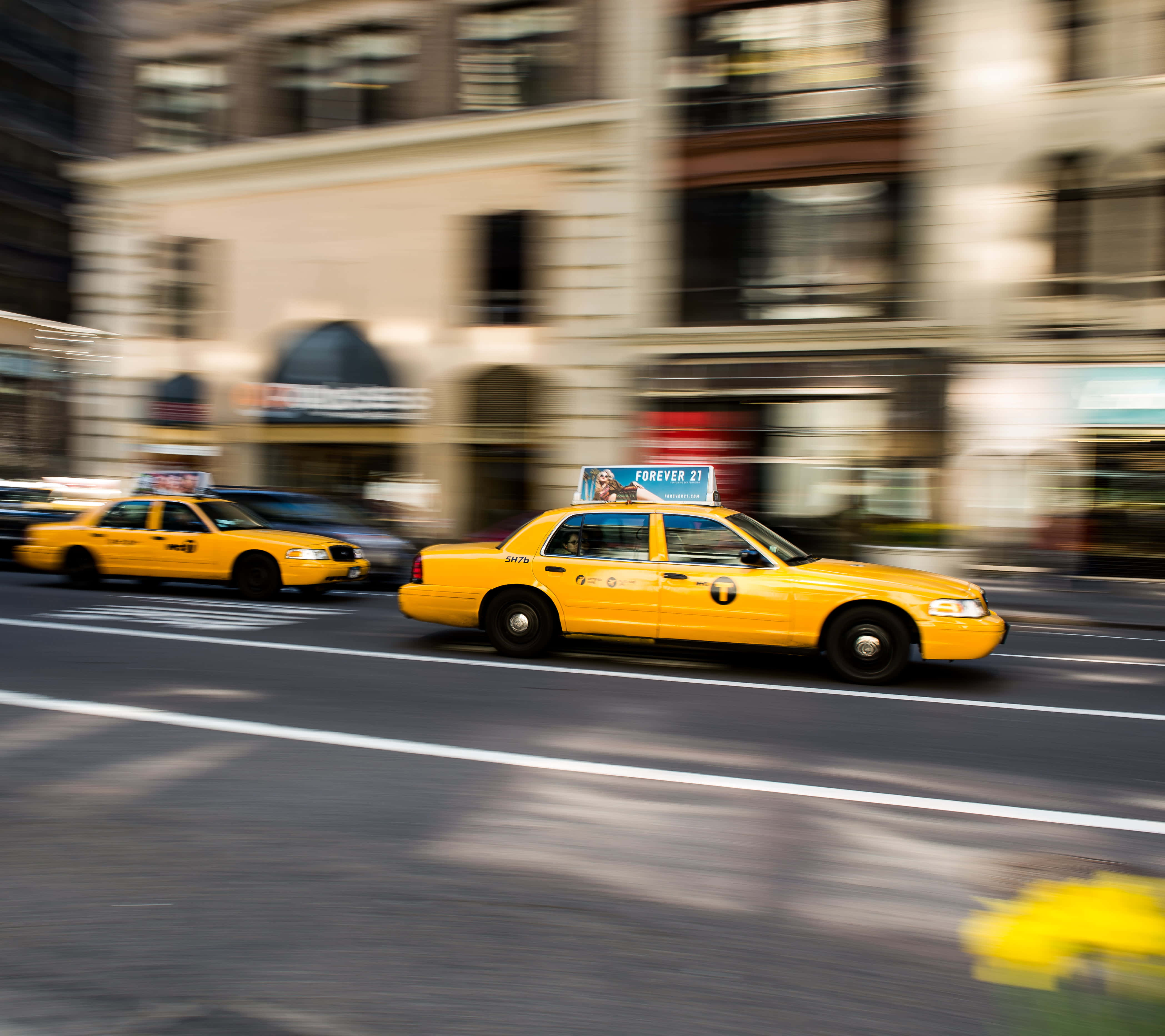 Yellow Cab 桌布 壁紙 — 充滿活力的黃色出租車在動感十足的都市街景中模糊地掠過城市建築。