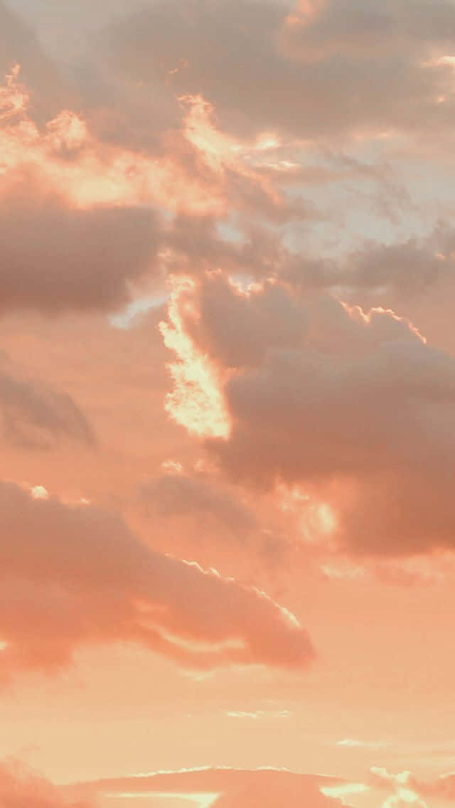 充滿美學雲朵的壯麗天空 壁紙 — 柔和的蜜桃色和粉紅色雲朵在昏暗的天空中溫暖地發光，微妙的陽光穿透雲層。