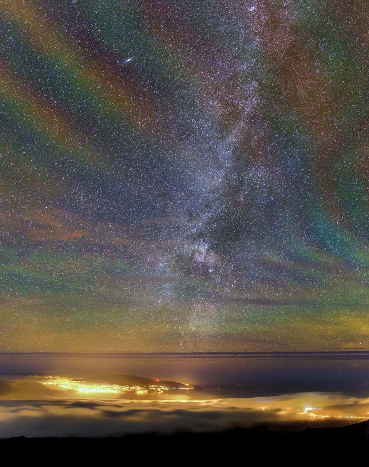 充滿色彩與生命的星河彩虹 壁紙 — 一個令人驚嘆的夜空，充滿星星和色彩繽紛的極光，拱形在發光的雲海之上，下方是遙遠的城市燈光。