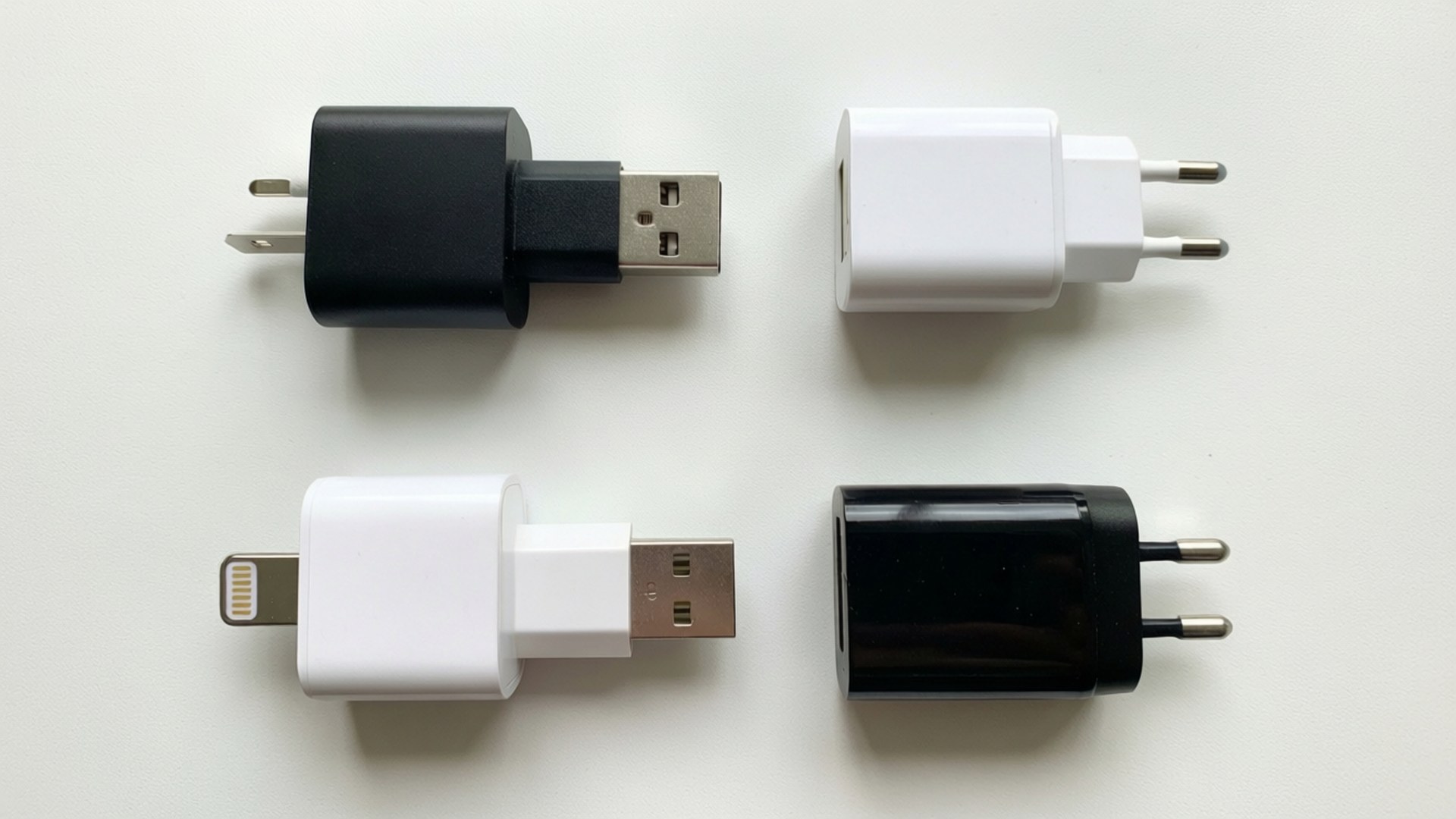 充電器系列 壁紙 — 四個黑白緊湊型手機充電器整齊排列在純白色表面上。