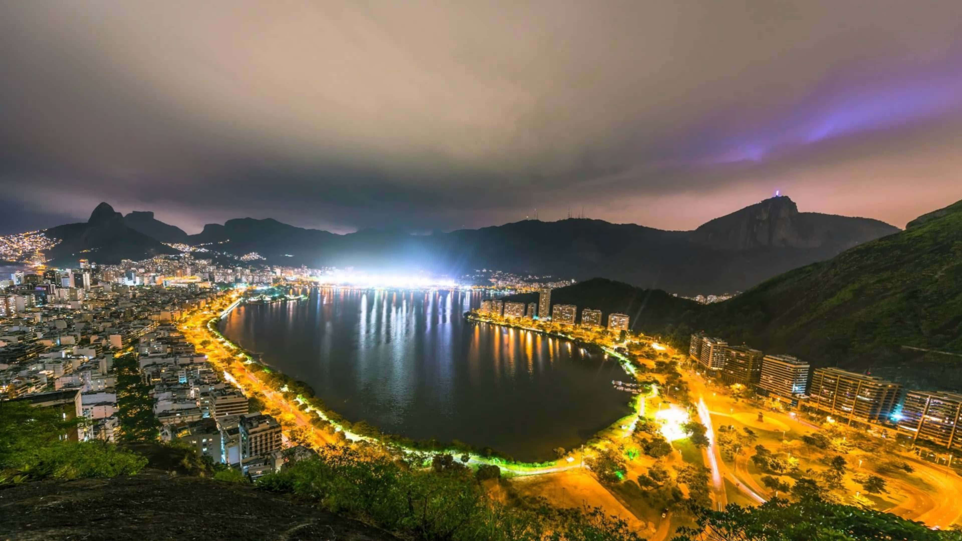 先進科技創新突破 壁紙 — 里約熱內盧海岸線充滿活力的夜景，城市燈光在水面上閃爍，背景是山脈。