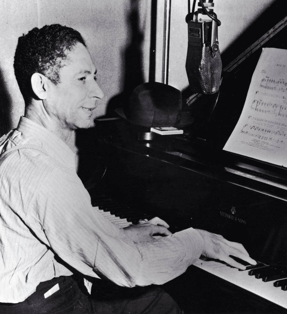 先驅爵士鋼琴家Jelly Roll Morton 壁紙 — 一名男子在復古錄音室彈鋼琴，附近有樂譜和麥克風。