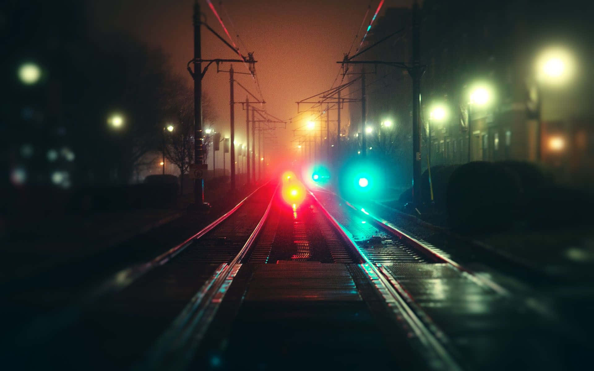火車燈光在夜霧中於潮濕軌道上閃爍紅綠光芒。