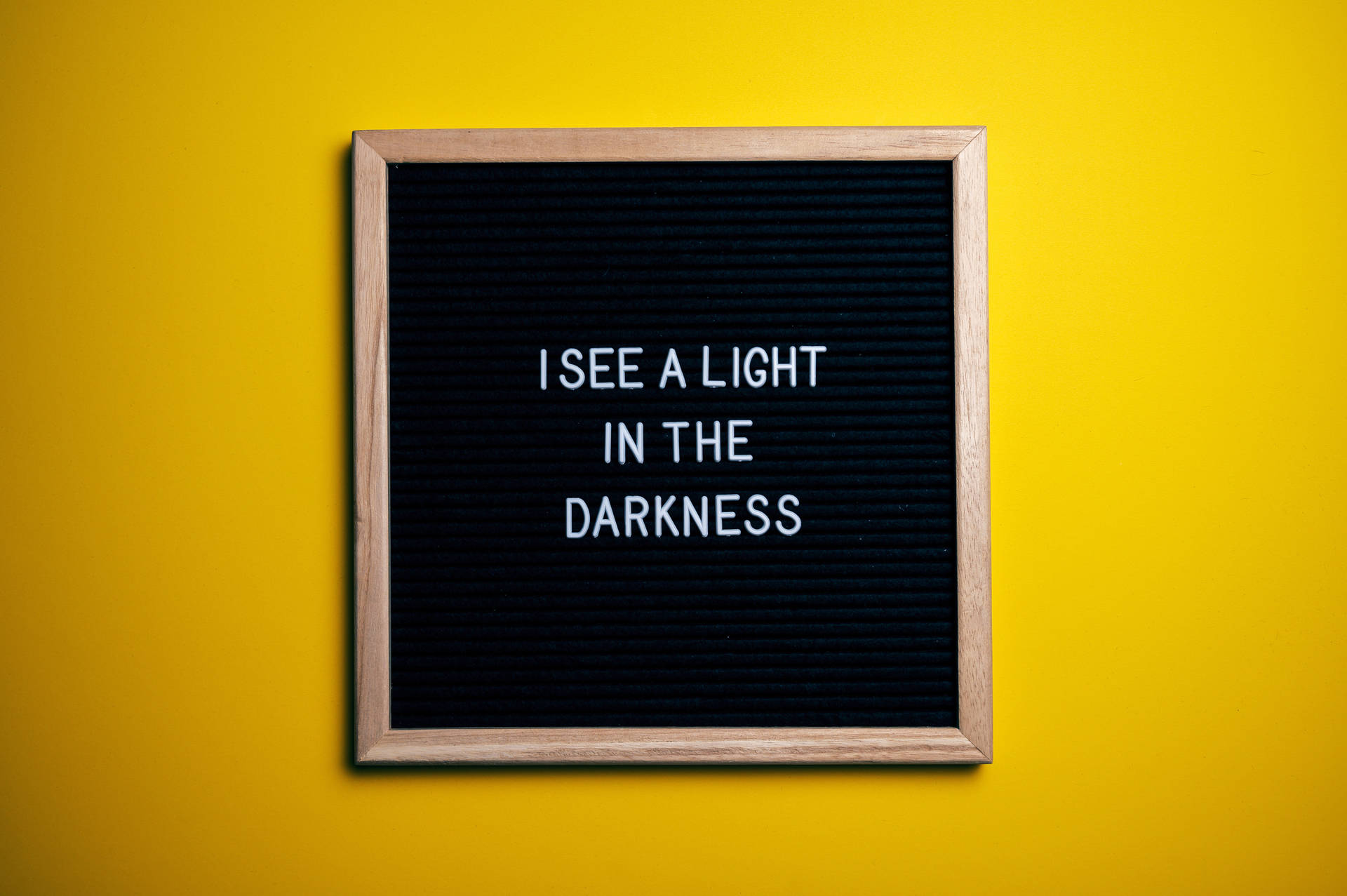 黃色牆上帶有訊息 I SEE A LIGHT IN THE DARKNESS 的字母板