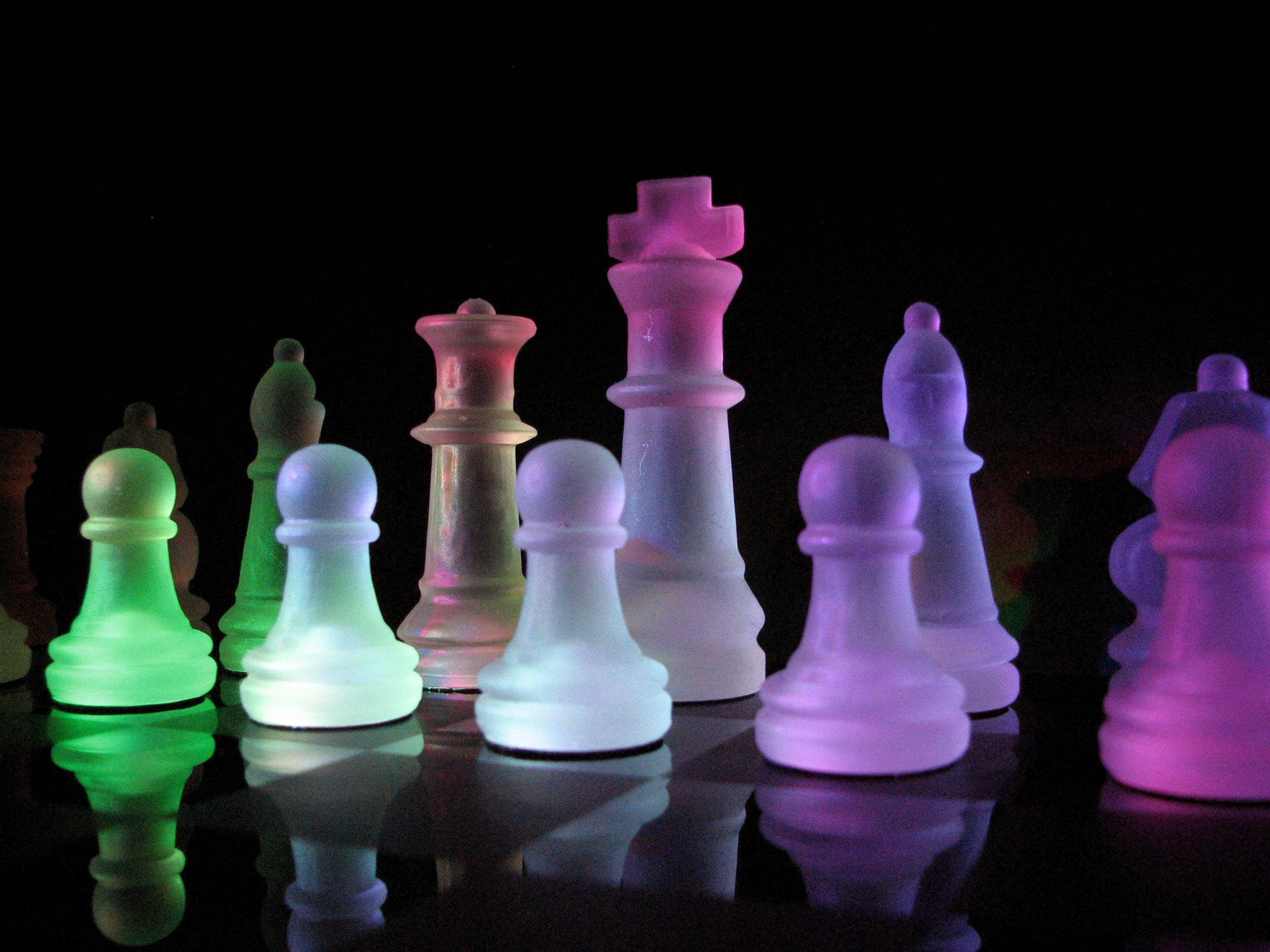 光暈磨砂棋子 壁紙 — 發光的半透明國際象棋棋子以鮮豔的霓虹色調立在黑色背景的反射表面上。
