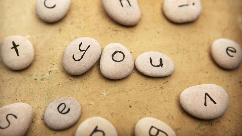 You 桌布 壁紙 — 光滑的石頭上以手寫字母拼出「thank you」，置於有紋理的米色表面上。