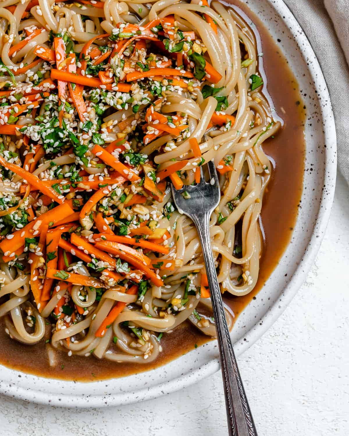 Noodles 桌布 壁紙 — 光澤烏冬麵配上美味醬汁，上面撒有紅蘿蔔絲、芝麻和切碎香草，盛在斑點碗中的特寫。