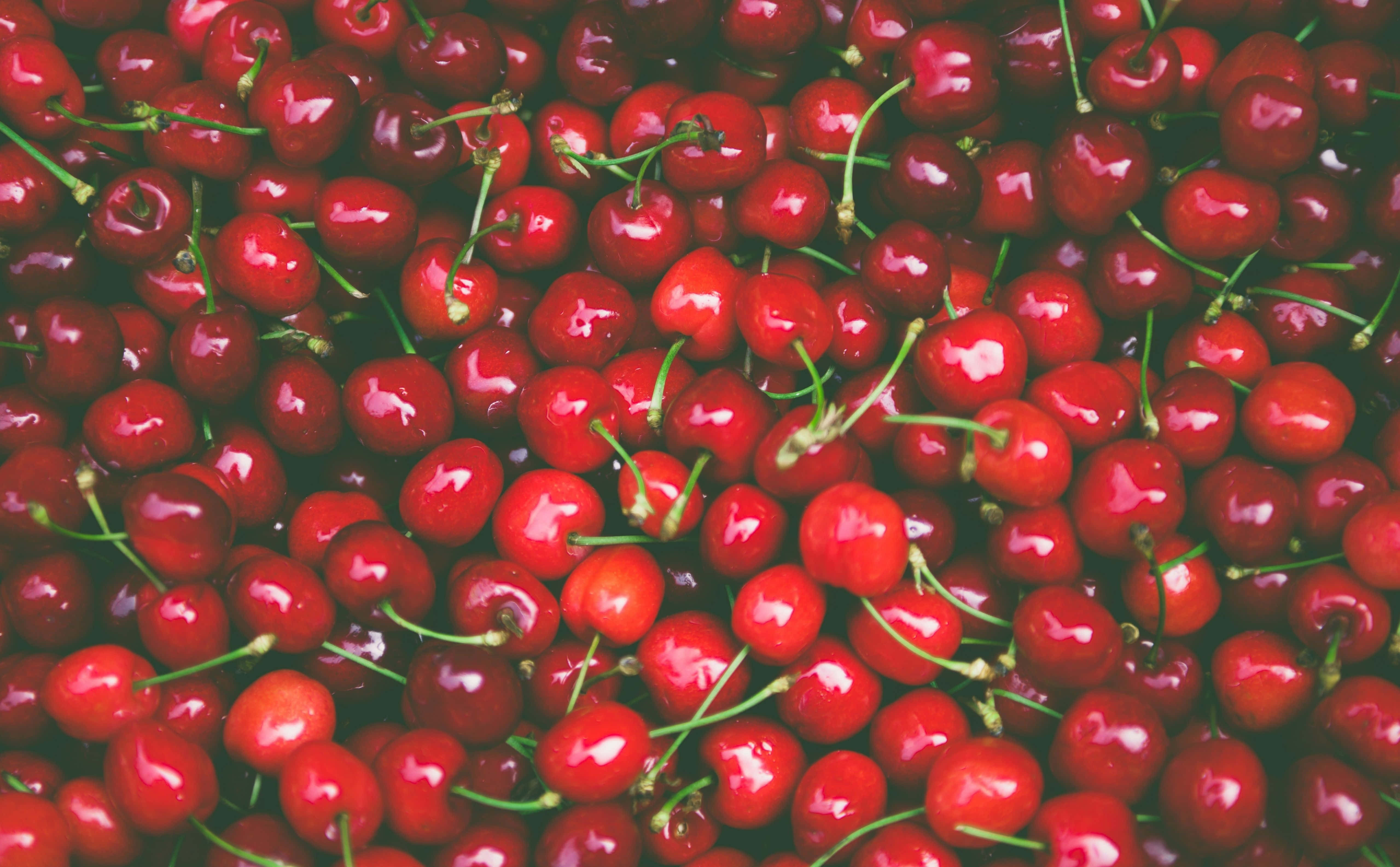 Cherry 桌布 壁紙 — 光澤紅色櫻桃的特寫，帶有綠色莖，密集堆疊在一起。