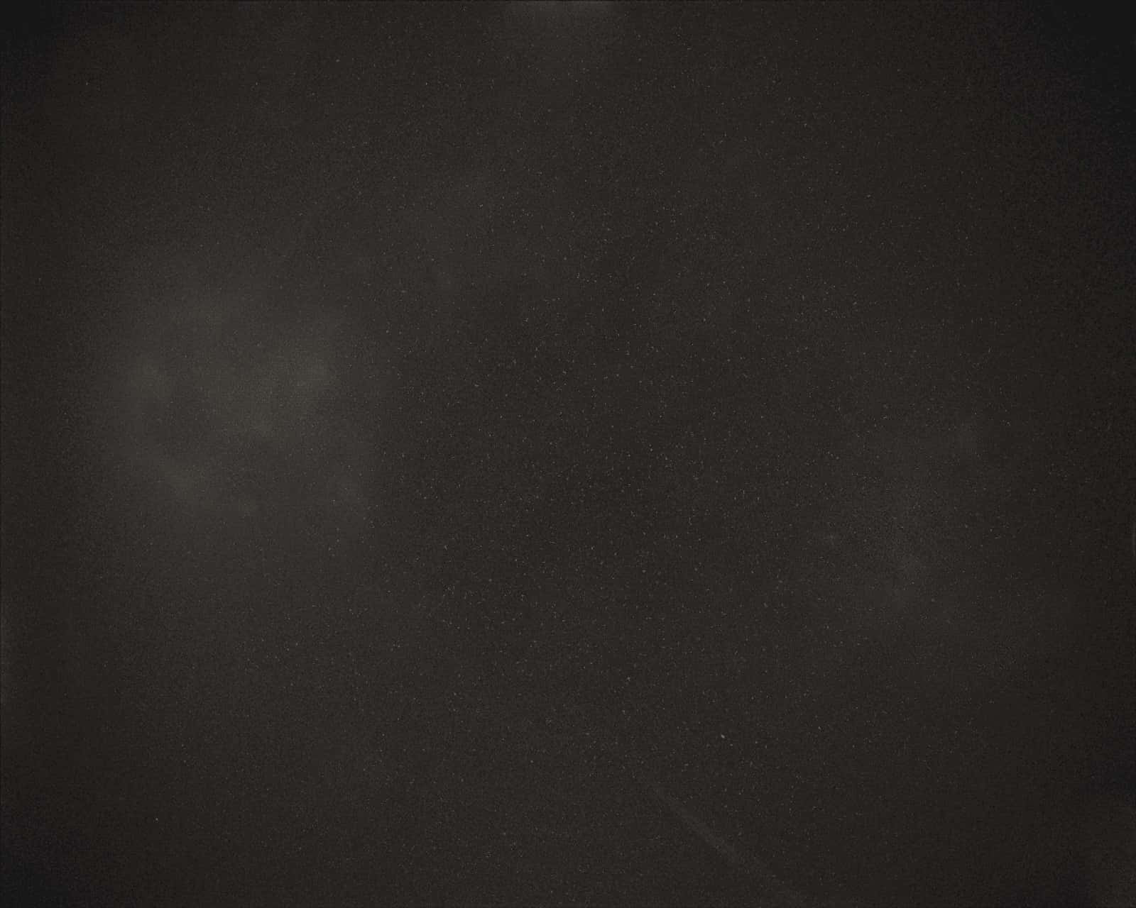 深色紋理表面，帶有灰色污跡和斑點，如老化的菲林或宇宙塵埃。