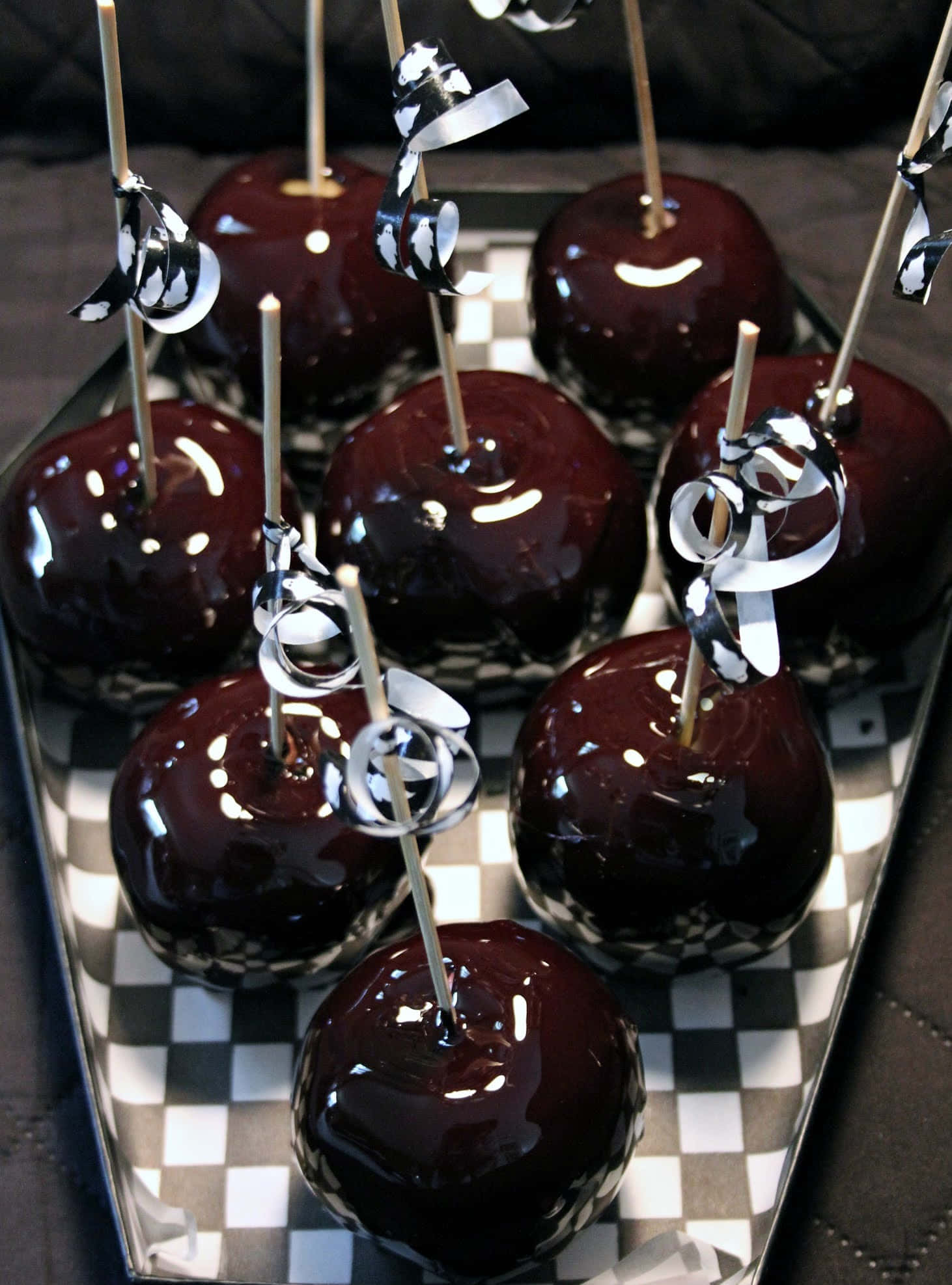 Candy Apples 桌布 壁紙 — 光澤黑巧克力焦糖蘋果，飾有銀色絲帶頂飾，排列在格子托盤上。