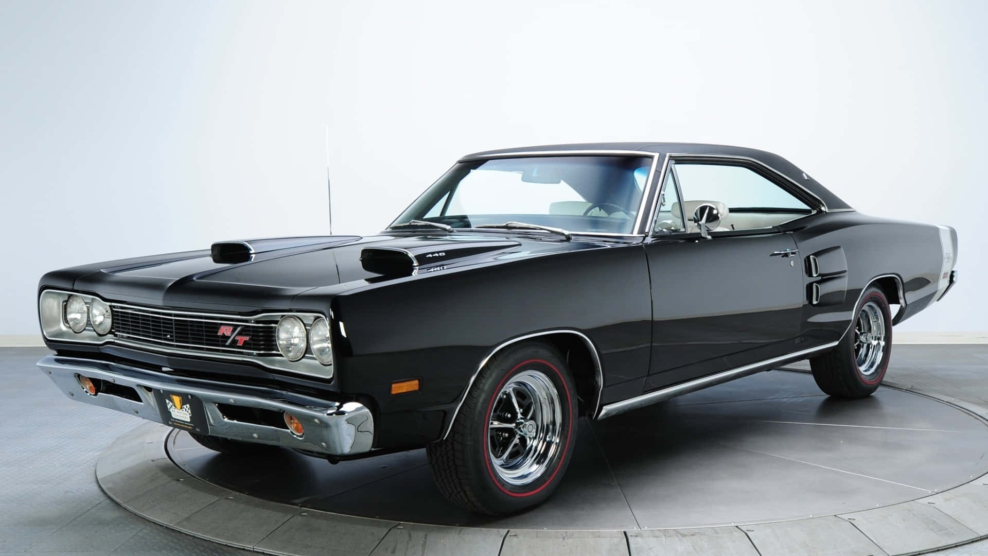 光澤黑色轎車，隨時出發 壁紙 — 一輛光澤黑色1960年代道奇Charger RT肌肉車，配備紅線輪胎和鍍鉻裝飾，放置在工作室轉盤上。