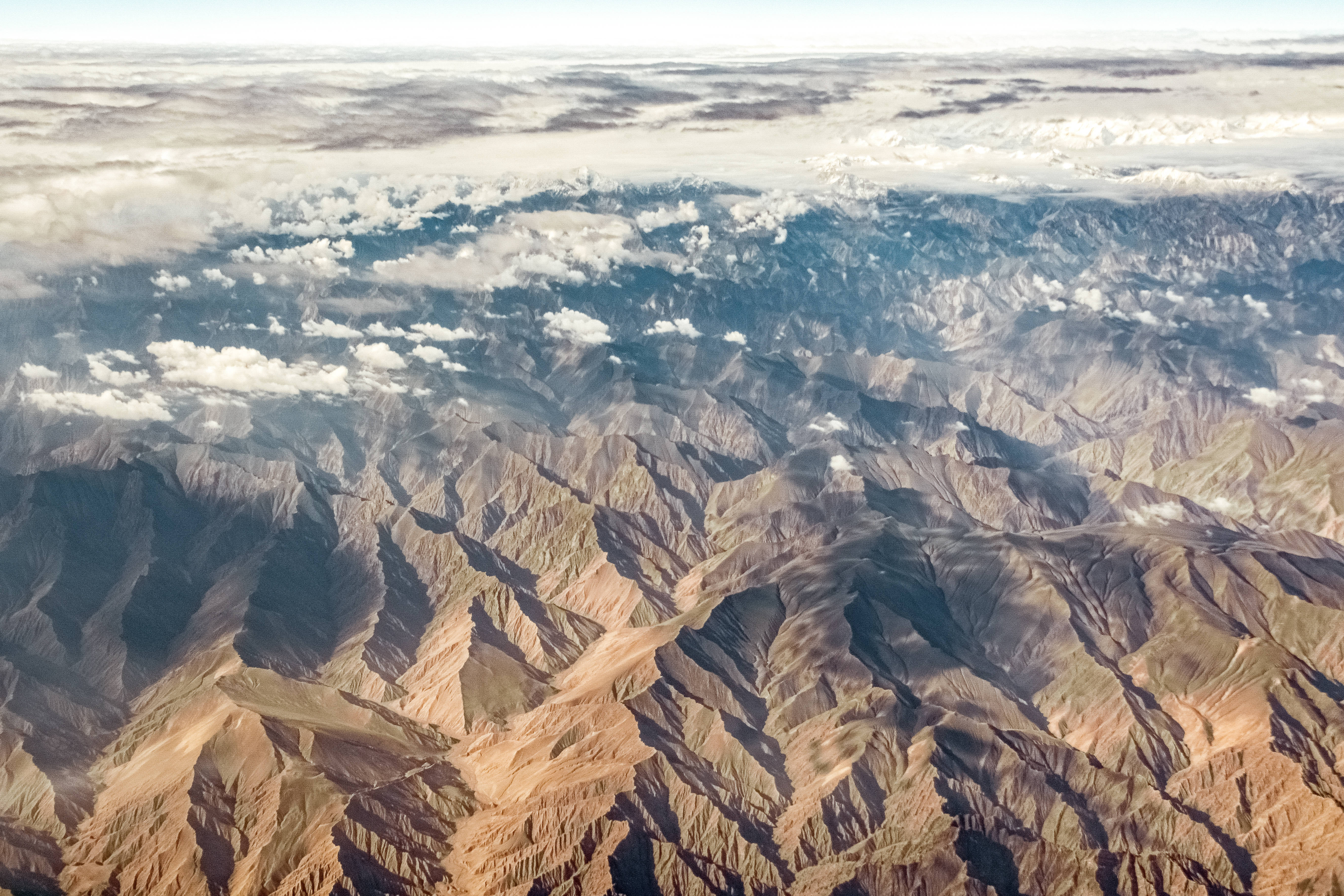 光禿山嶺地貌 壁紙 — 崎嶇山脈的鳥瞰圖，有深谷和下方散落的雲層。