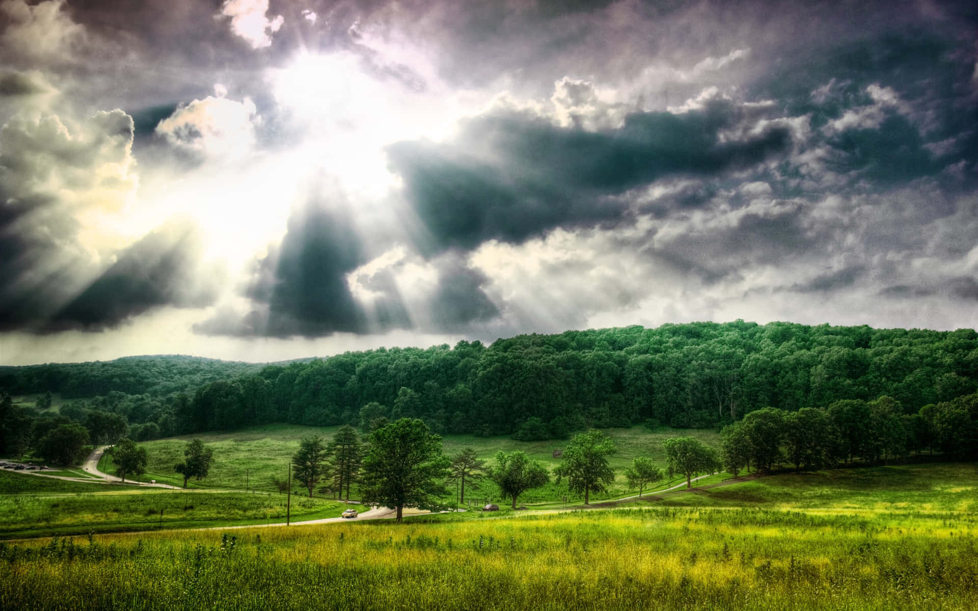 陽光穿過暴風雲，照耀在一個有樹木和丘陵的綠色山谷上。