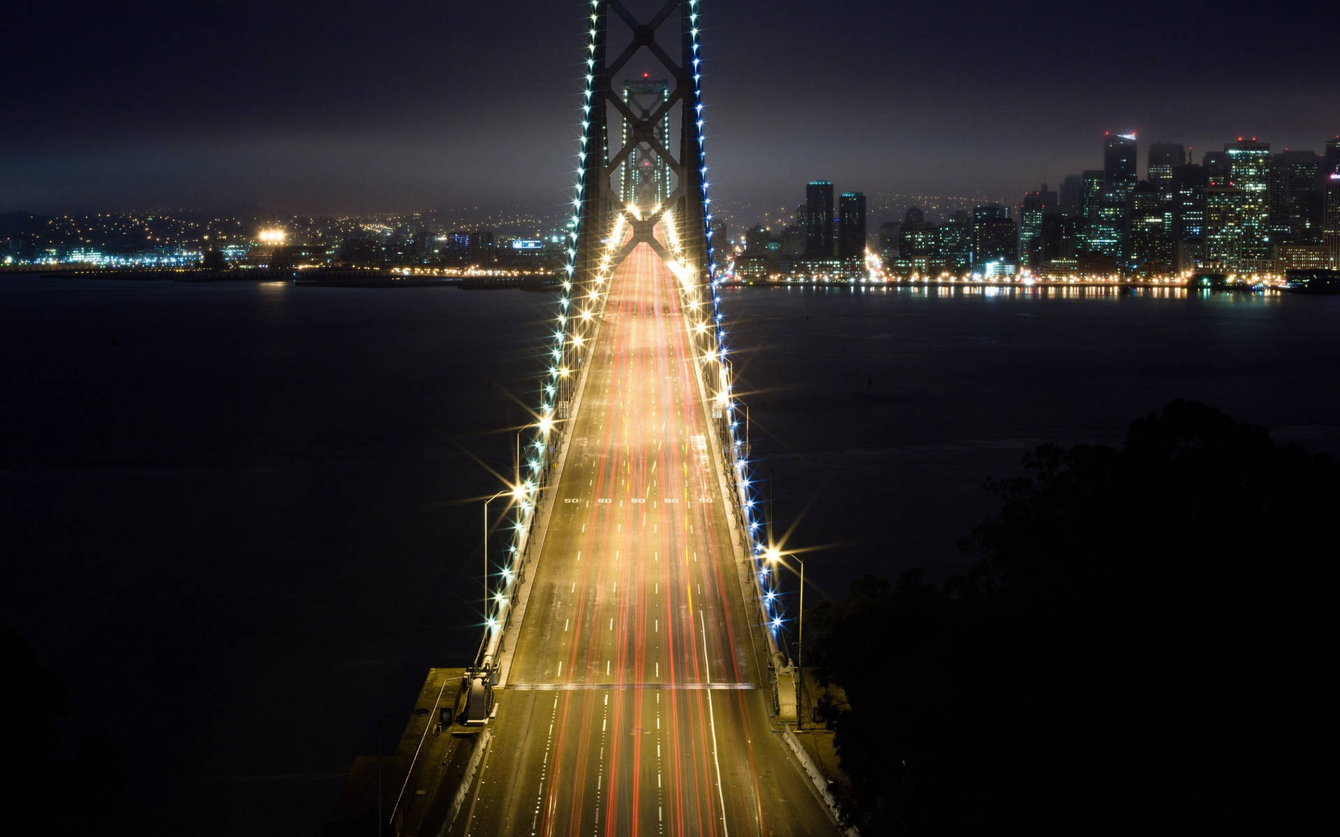 夜間的橋樑，帶有汽車燈光軌跡和背景的城市天際線。