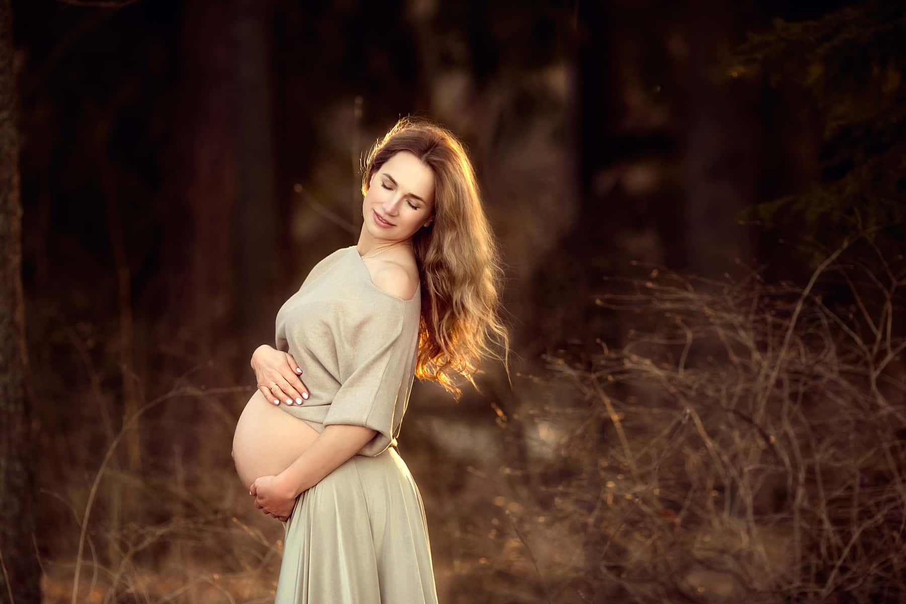 孕婦在陽光明媚的森林中輕柔地抱著腹部。