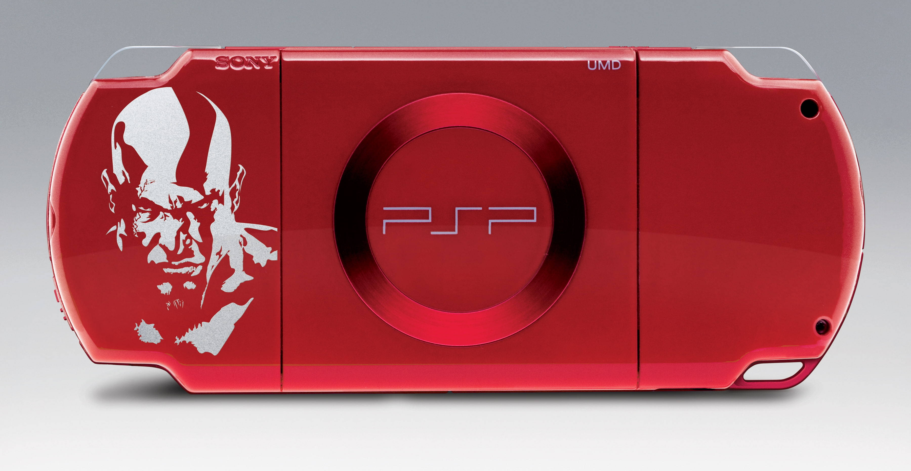 God Of War 桌布 壁紙 — 光面紅色Sony PSP主機，帶有白色Kratos面部貼紙和圓形標誌，背景為中性灰色。