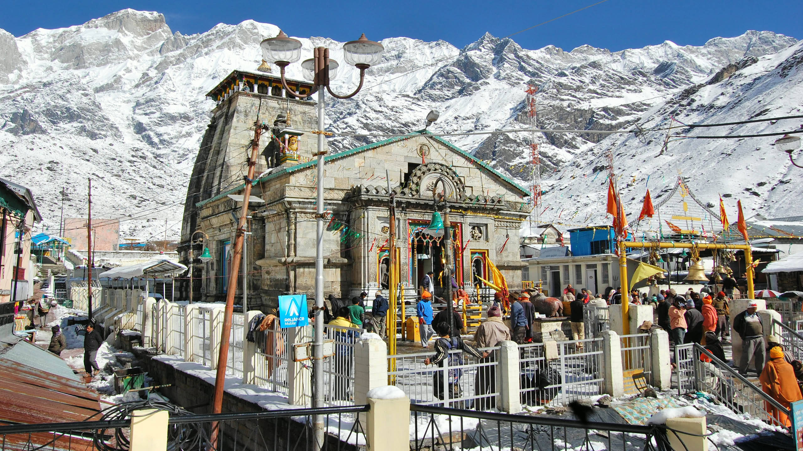 克德納特寺廟圍欄4K 壁紙 — 熱鬧的雪覆蓋寺廟坐落在雄偉的喜馬拉雅山脈下，天空清澈湛藍。