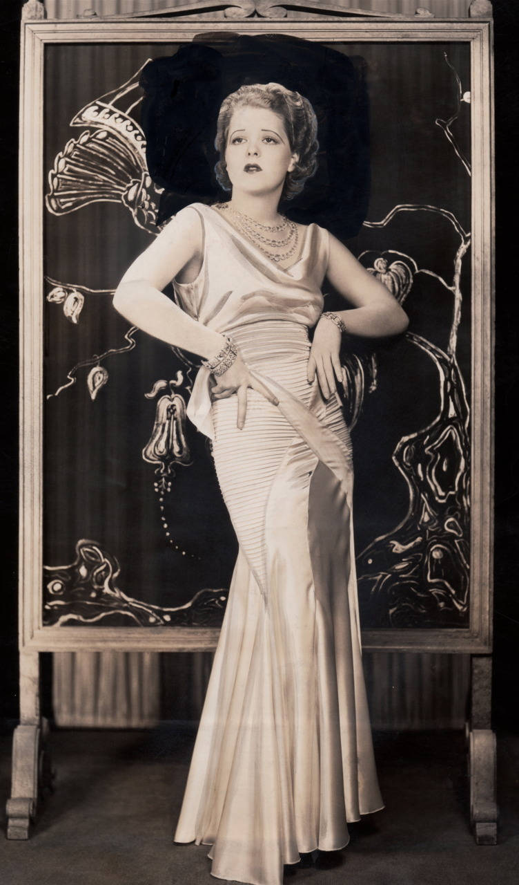 克拉拉·鮑絲綢禮服 壁紙 — 一位穿著垂墜絲綢長袍的1920年代迷人女性，在帶有風格化花卉圖案的華麗屏風前優雅地擺姿勢。