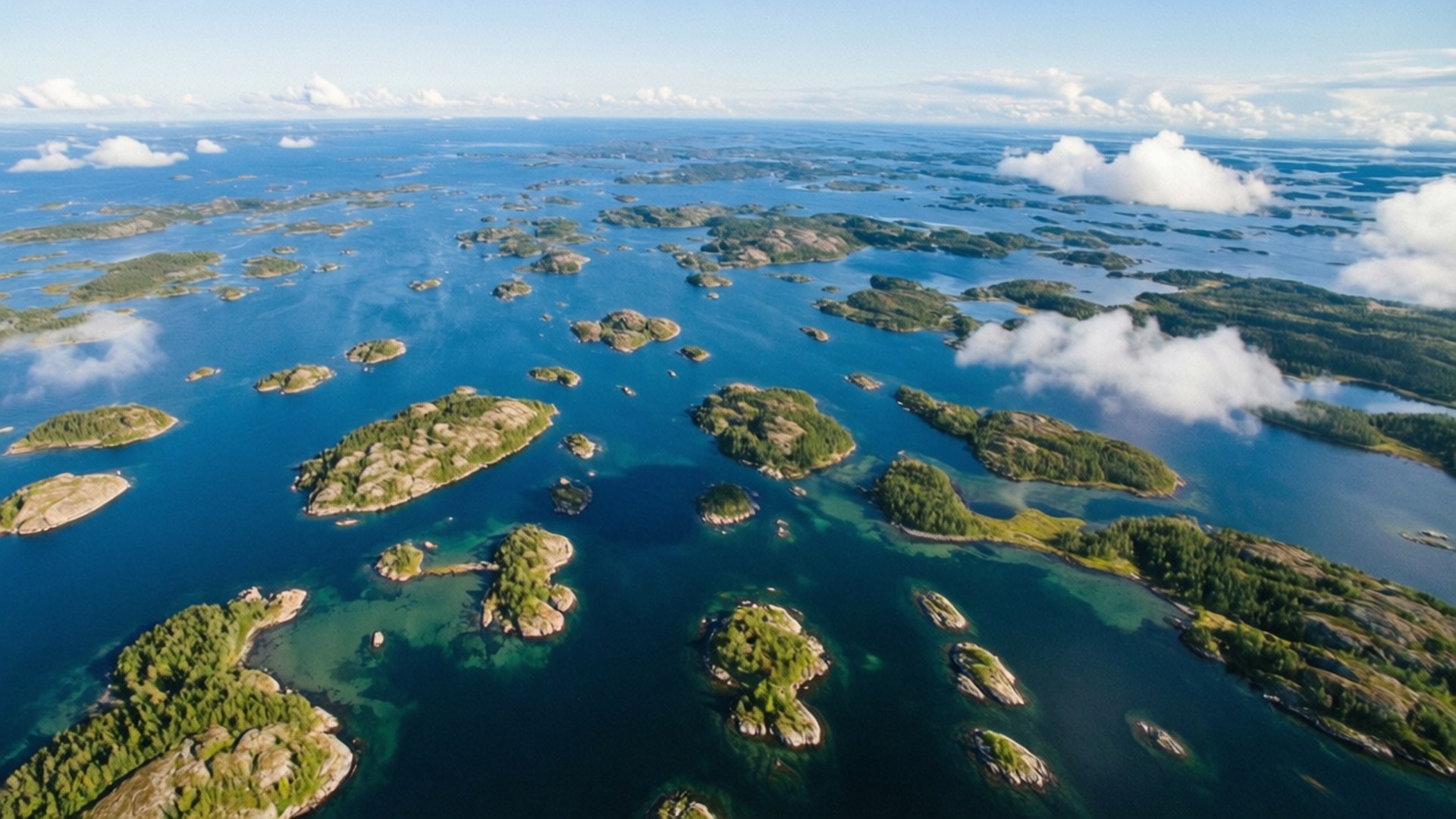 從空中俯瞰，許多森林覆蓋的小島在藍色水域中，有白雲