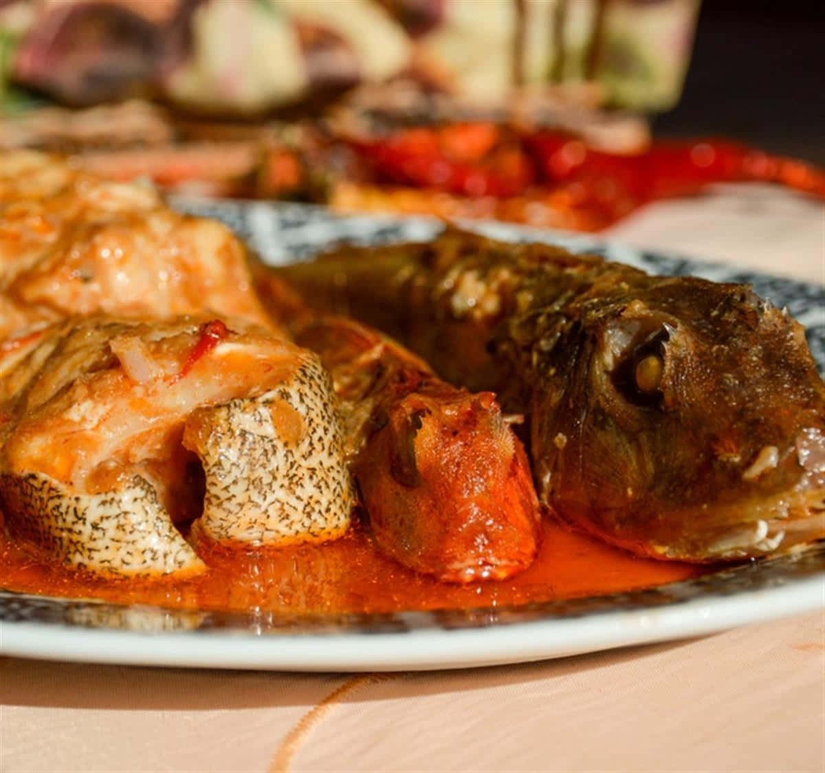 克羅地亞布魯德特魚肉特寫 壁紙 — 特寫鏡頭：一條完整烹調的魚，配上濃郁的紅醬，放在有圖案的碟子上。
