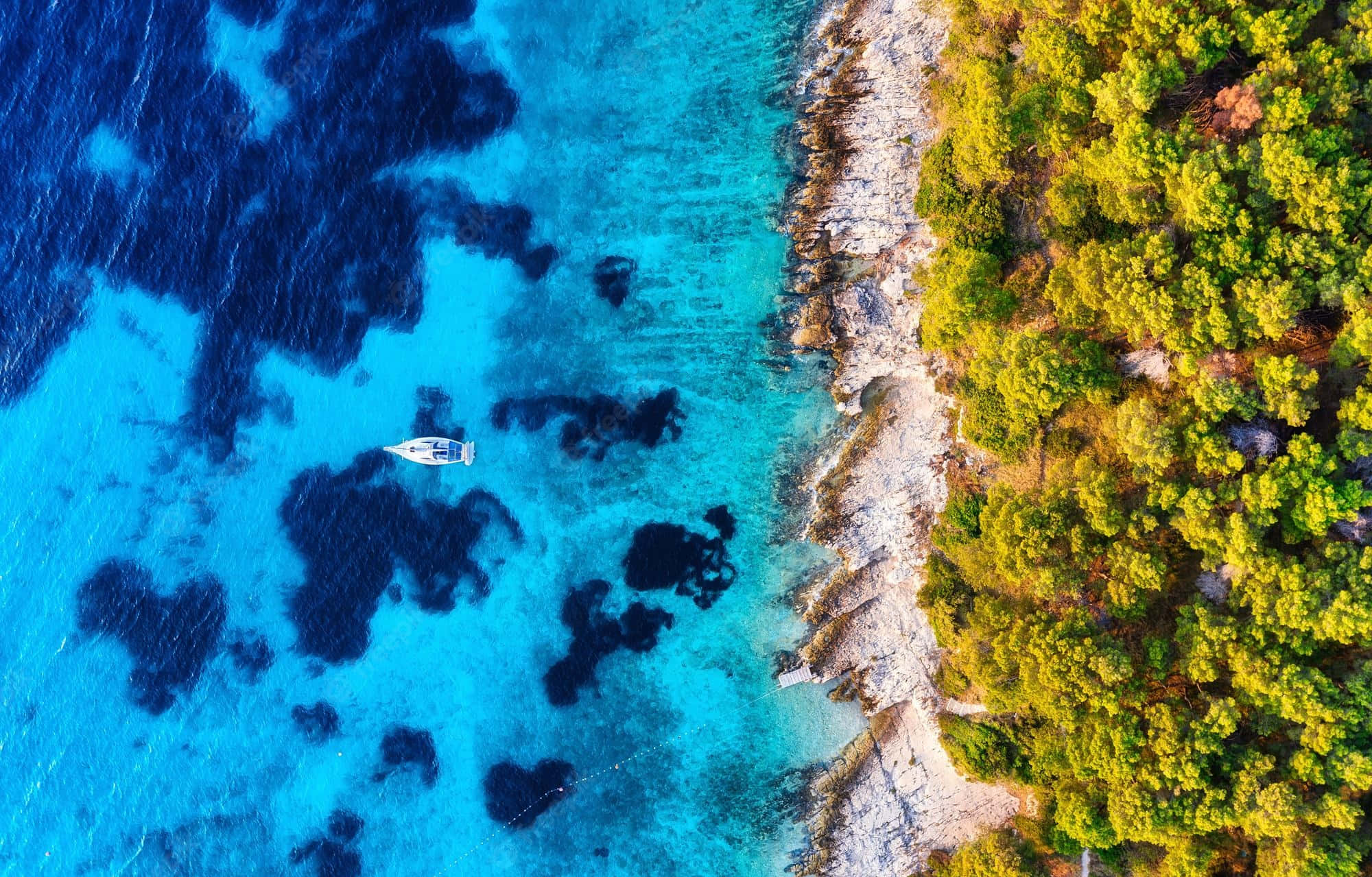 克羅地亞陸海交界 壁紙 — 從空中俯瞰，一艘孤獨的帆船在充滿活力的碧綠海水上漂流，旁邊是茂密綠色森林環繞的岩石海岸。