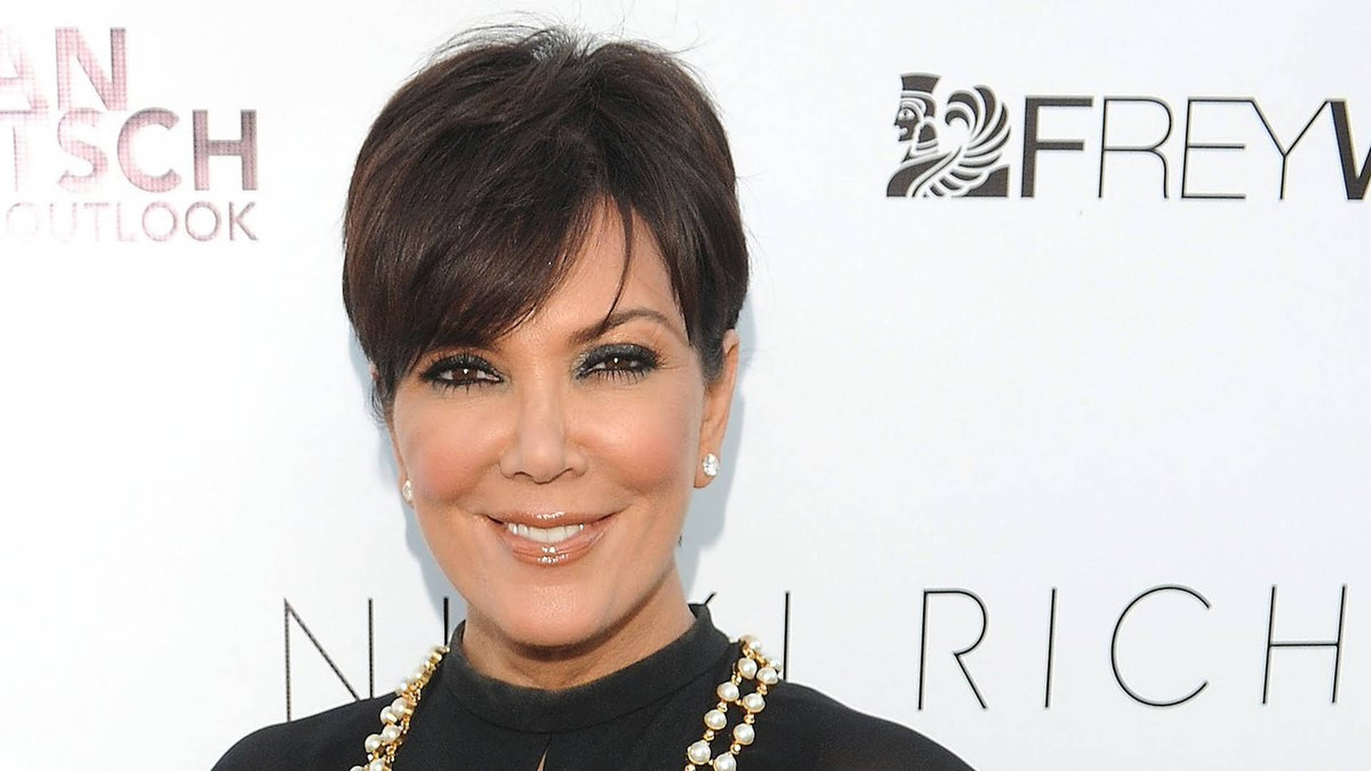Kris Jenner 在活動中穿著黑色上衣和珍珠項鍊微笑。