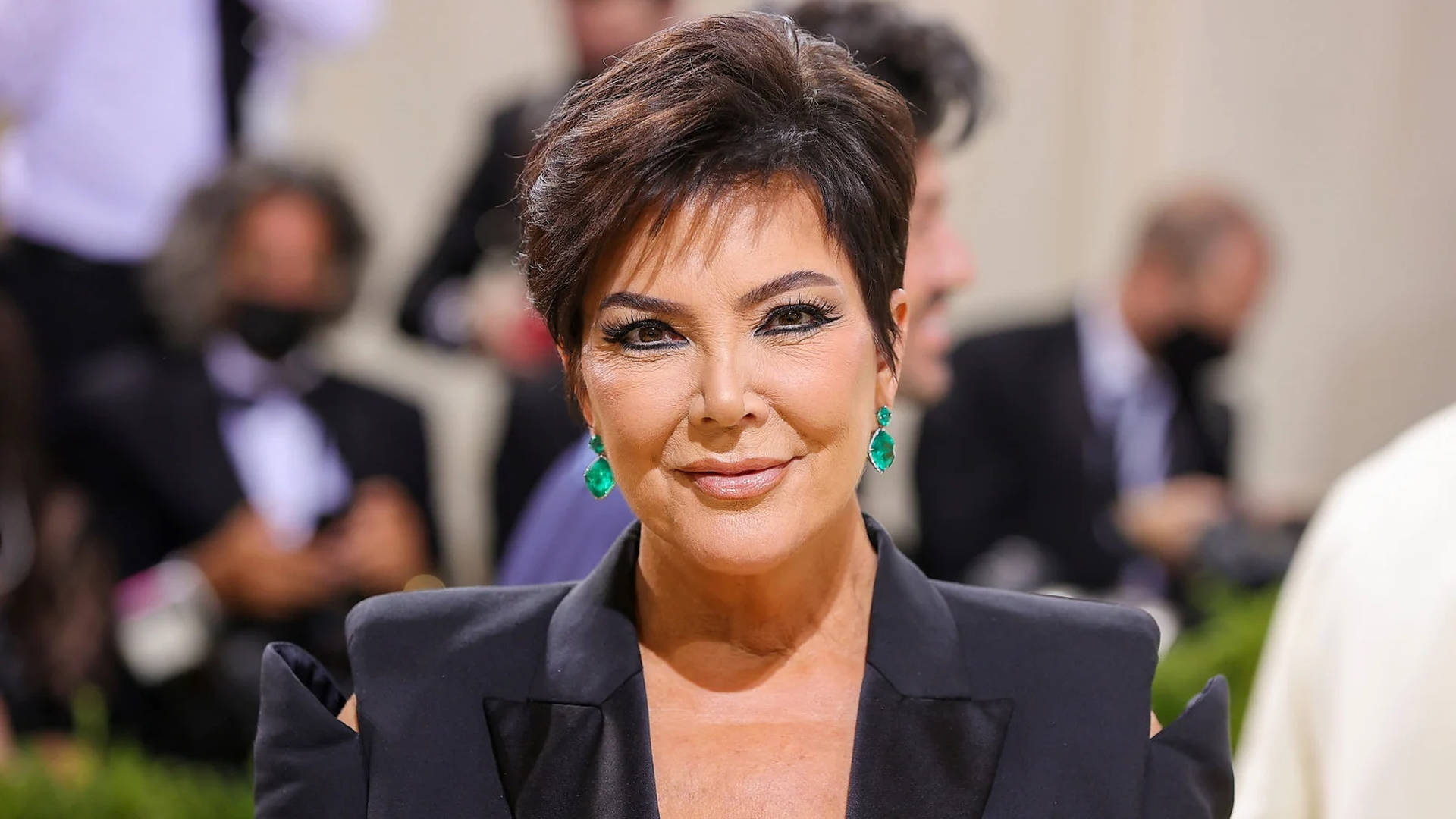 Kris Jenner 喺正式活動中身穿黑色西裝外套，配戴綠色耳環。